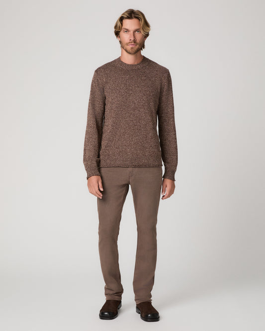 A man modeling a brown textured knit crewneck sweater and matching brown trousers paired with brown shoes against a light gray studio background.