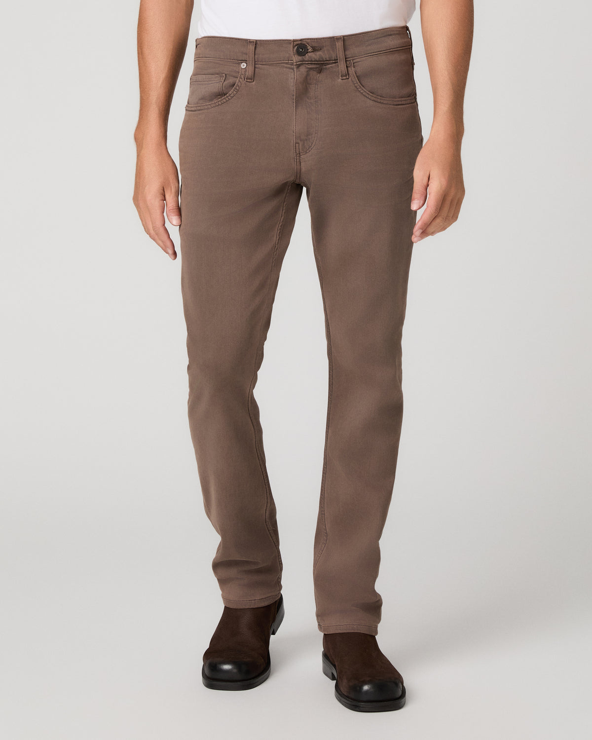 A man modeling a white tee and matching brown trousers paired with brown shoes against a light gray studio background.