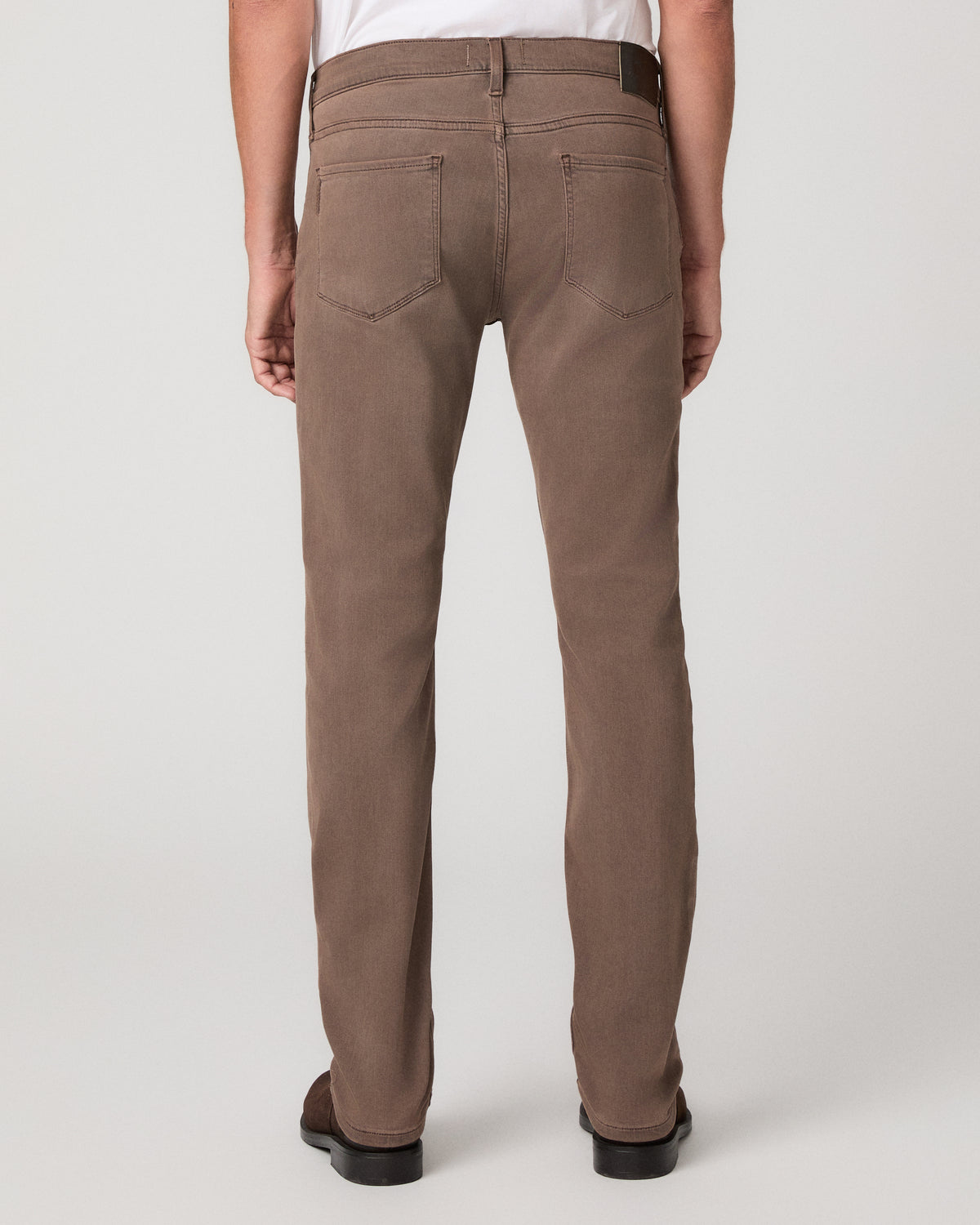 A man modeling a white tee and matching brown trousers paired with brown shoes against a light gray studio background.