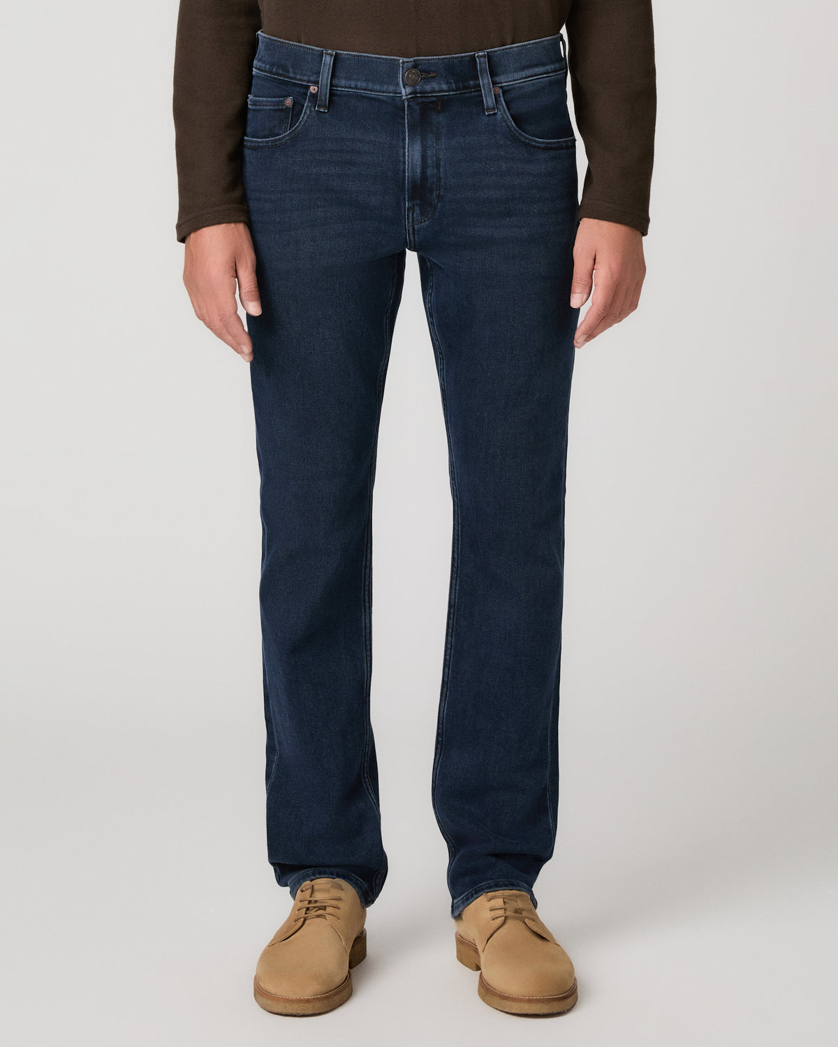 A man modeling a dark brown long-sleeve knit polo shirt, paired with dark blue jeans and tan suede boots, against a light gray studio background.