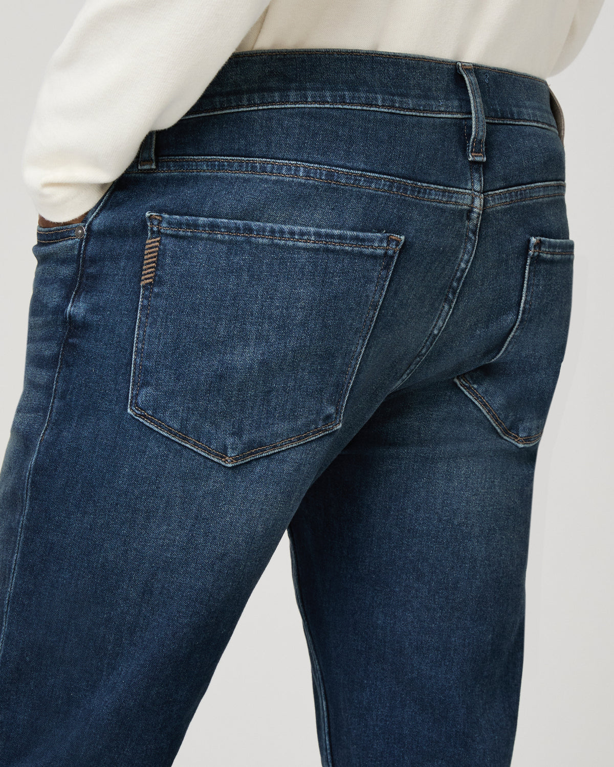 Close-up of the back pocket detailing on the medium-dark wash denim, hand resting near the hip pocket.