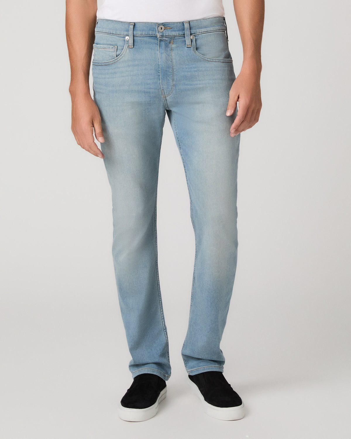 A man modeling a white tee paired with light blue jeans and black sneakers, standing against a light gray studio background.