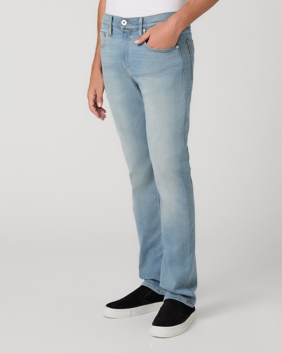 A man modeling a white tee paired with light blue jeans and black sneakers, standing against a light gray studio background.