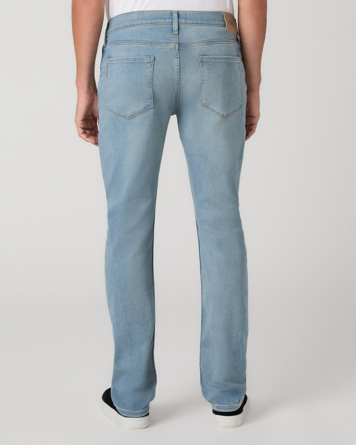 A man modeling a white tee paired with light blue jeans and black sneakers, standing against a light gray studio background.