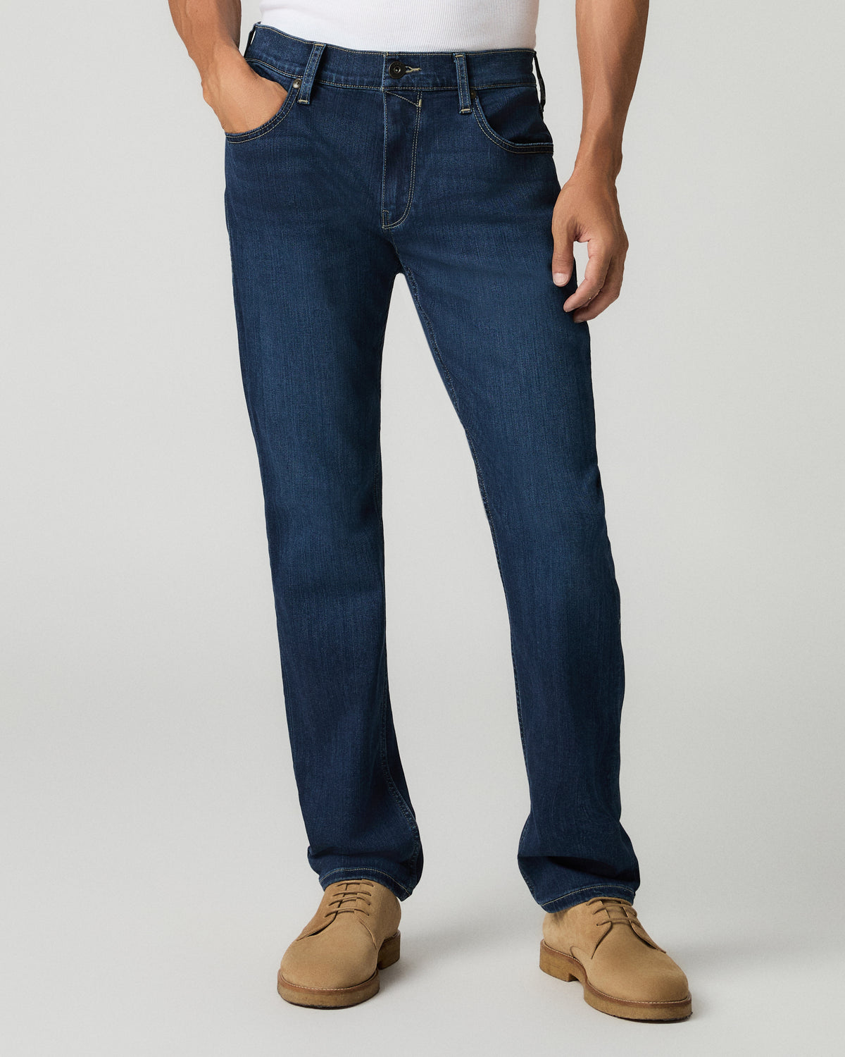 Close-up front view of a man with one hand in his pocket wearing deep blue slim-straight jeans, white t-shirt visible above the waistband.