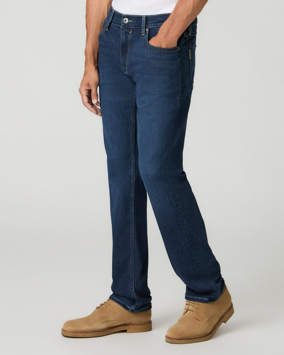 Side profile view from the waist down of a man wearing deep blue slim-straight jeans, paired with tan suede shoes.