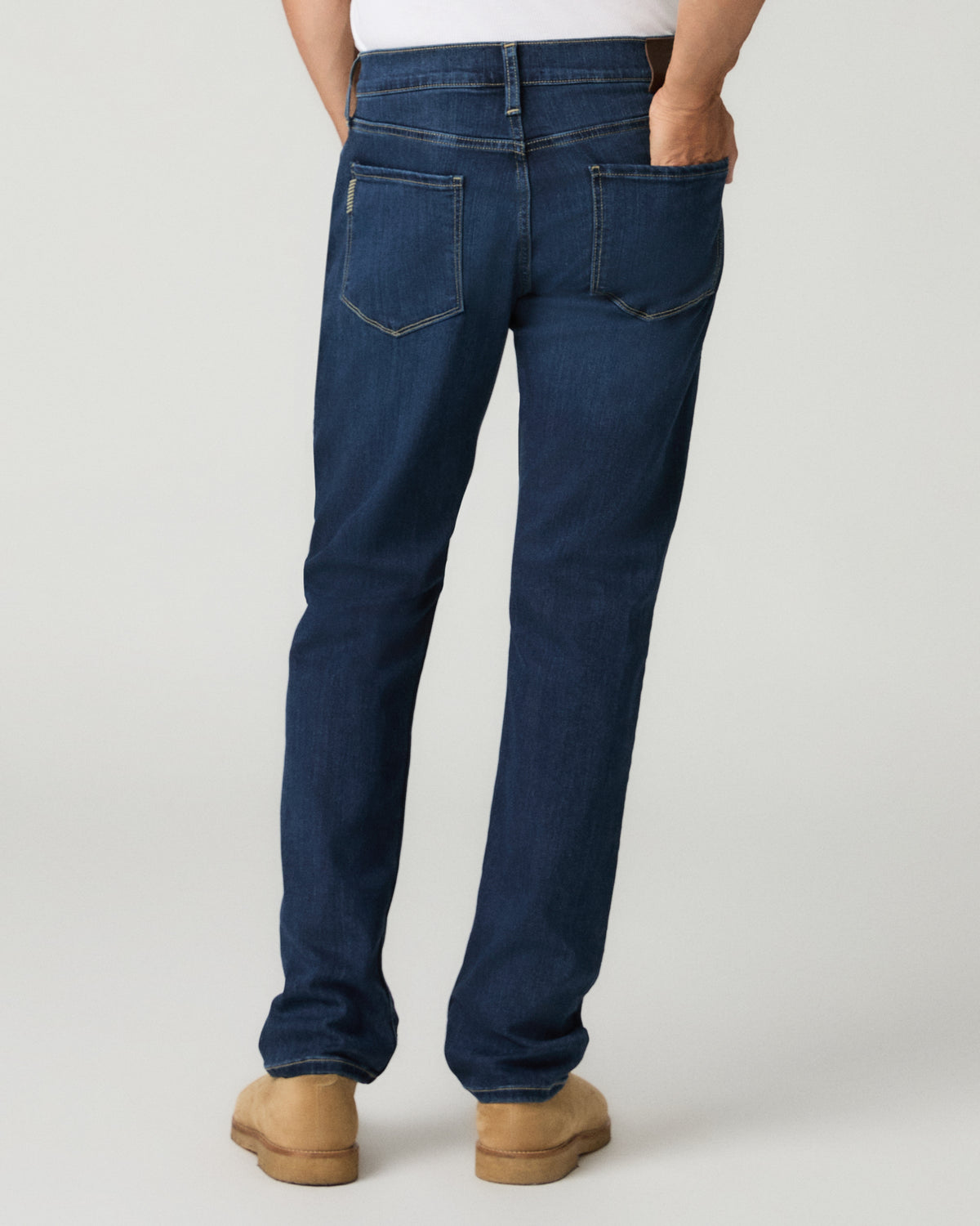 Full-length back view of a man wearing deep blue slim-straight jeans with tan suede shoes.