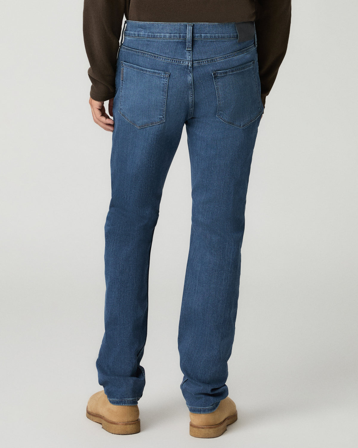 Full-length back view of a man wearing medium blue slim-straight jeans with tan suede shoes.