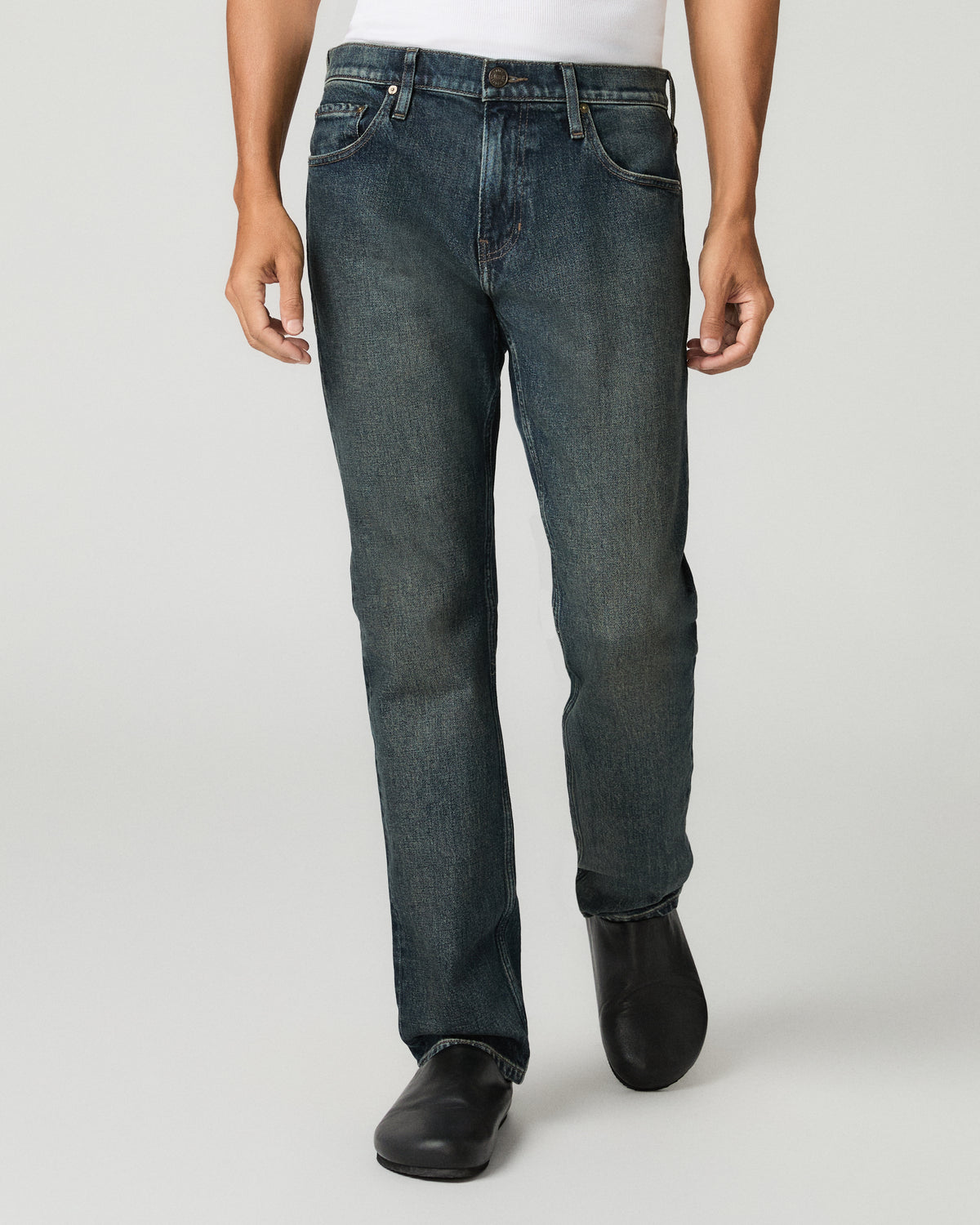 Close-up front view of a man with hands in his pockets wearing charcoal slim-straight jeans with a white t-shirt visible above the waistband.