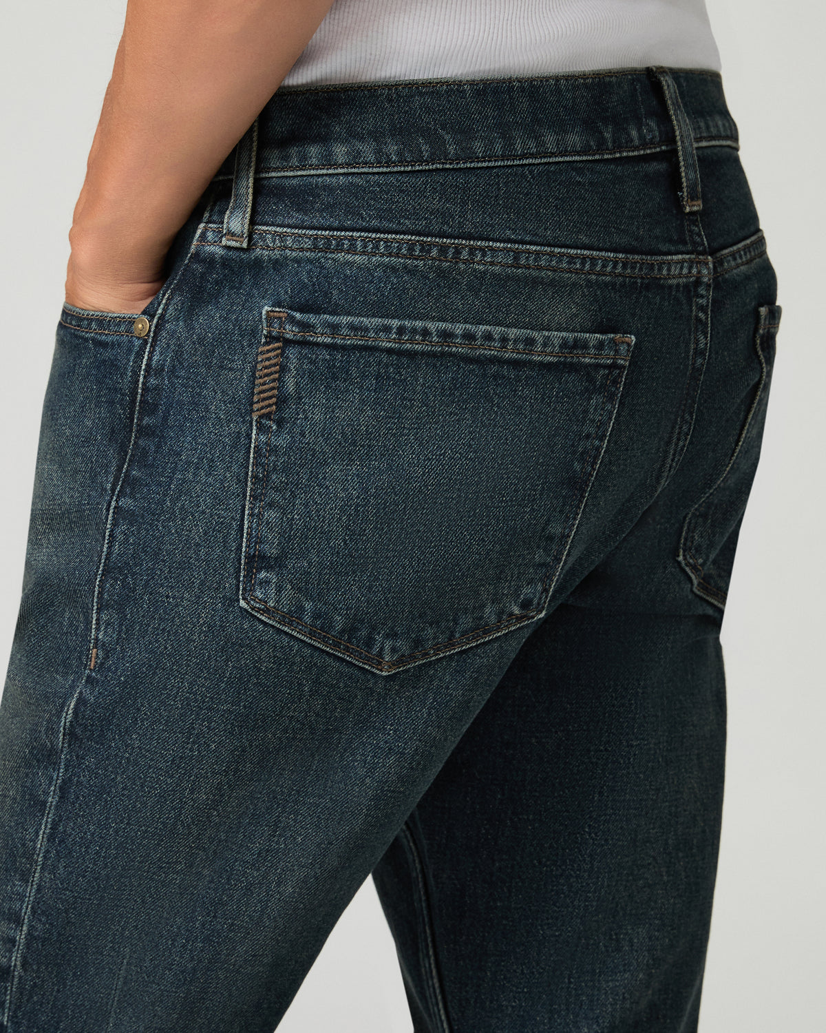 Close-up back pocket detail of charcoal slim-straight jeans, showing a leather brand patch and contrast stitching.
