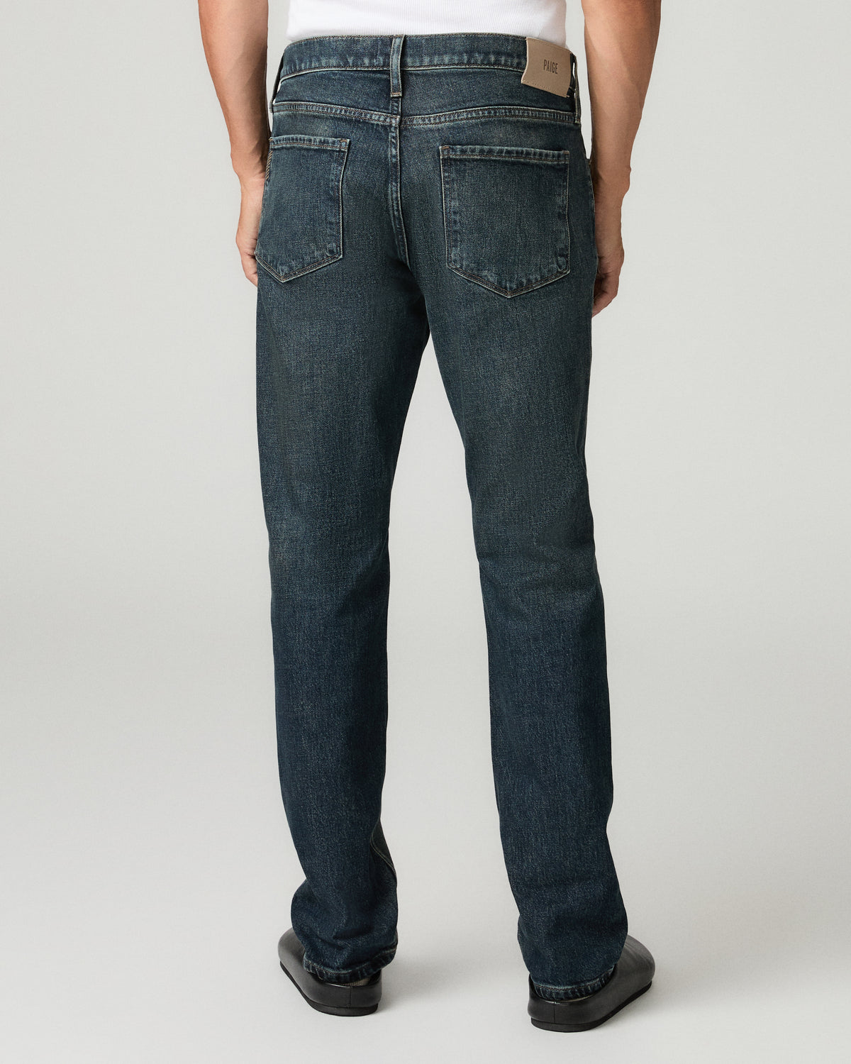 Full-length back view of a man wearing a white t-shirt and charcoal slim-straight jeans with black leather loafers.
