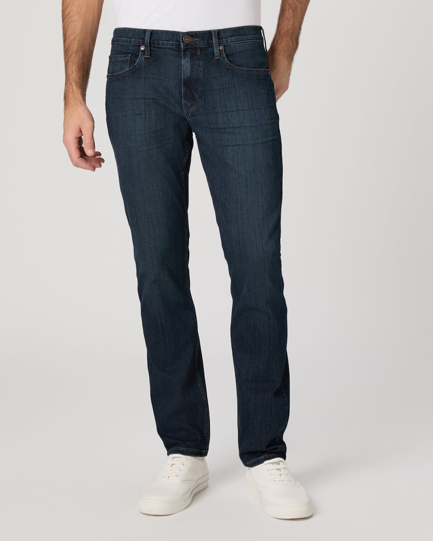 Man wearing a white t-shirt, dark jeans, and white shoes on a white background