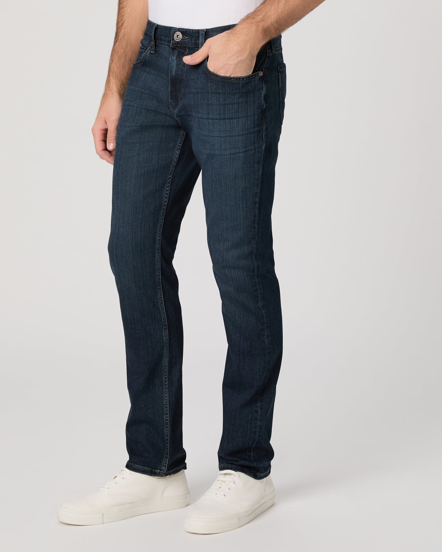 Man wearing a white t-shirt, dark jeans, and white shoes on a white background