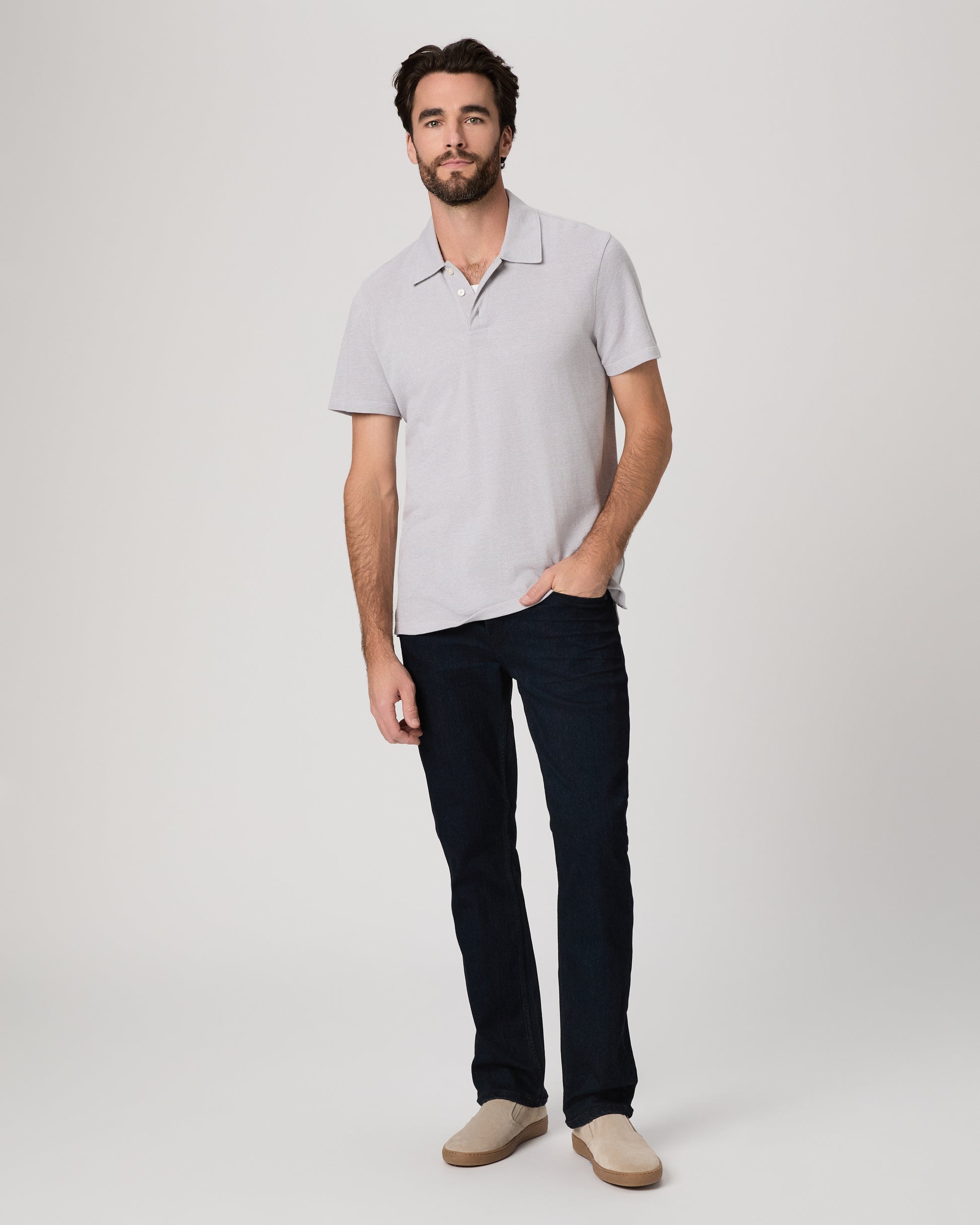 Man wearing a light gray polo shirt and dark jeans on a white background