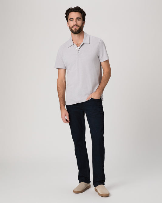 Man wearing a light gray polo shirt and dark jeans on a white background