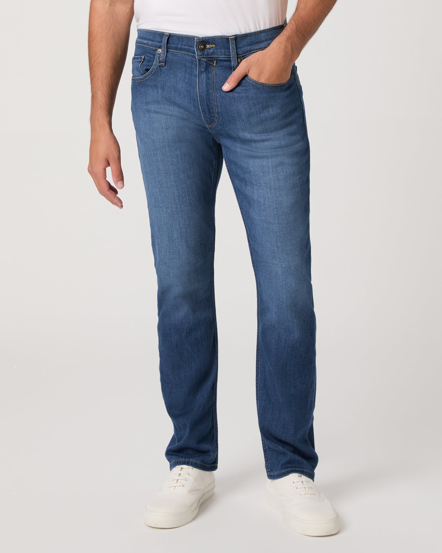 Man wearing a white shirt, blue jeans, and white shoes on a white background