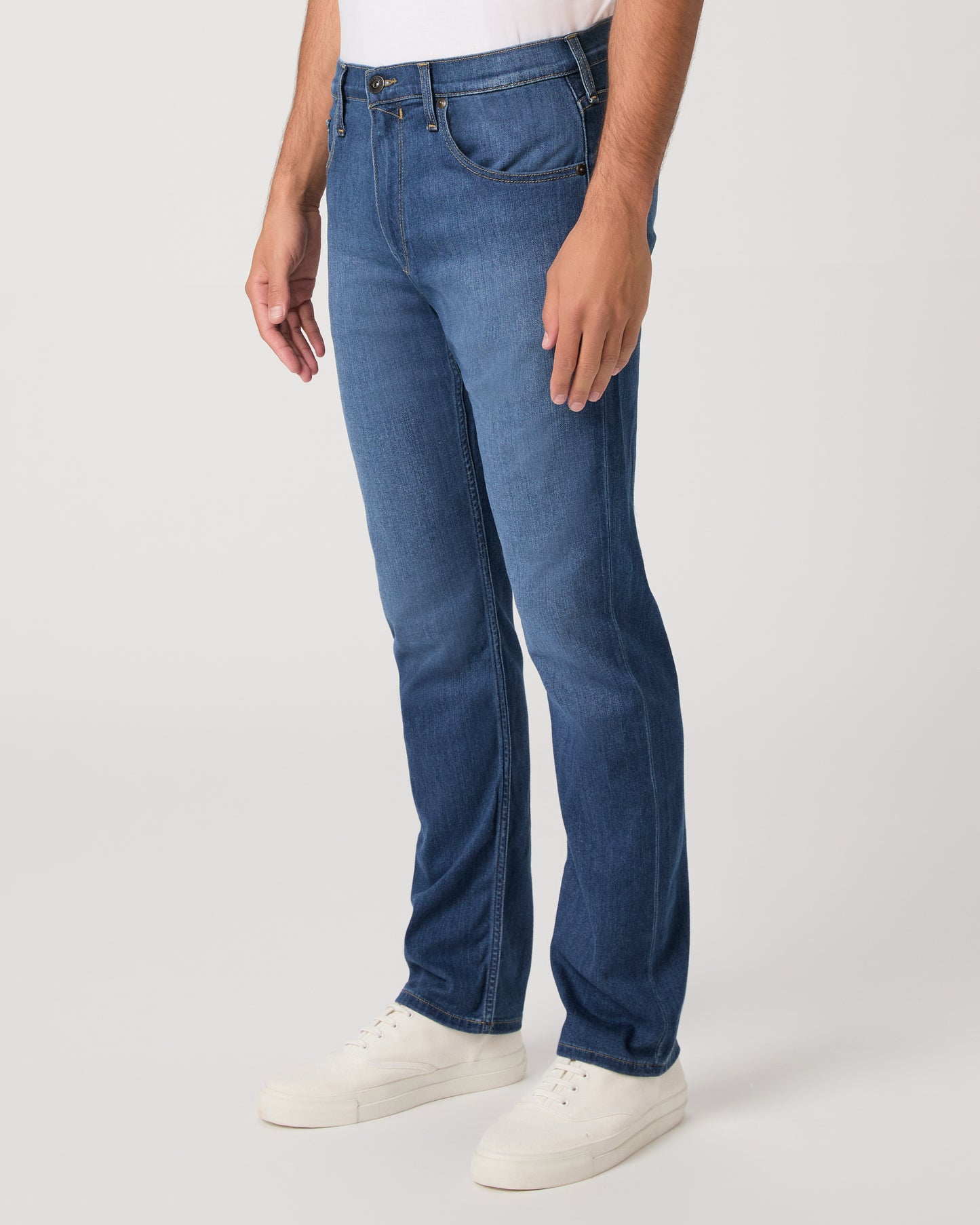 Man wearing a white shirt, blue jeans, and white shoes on a white background