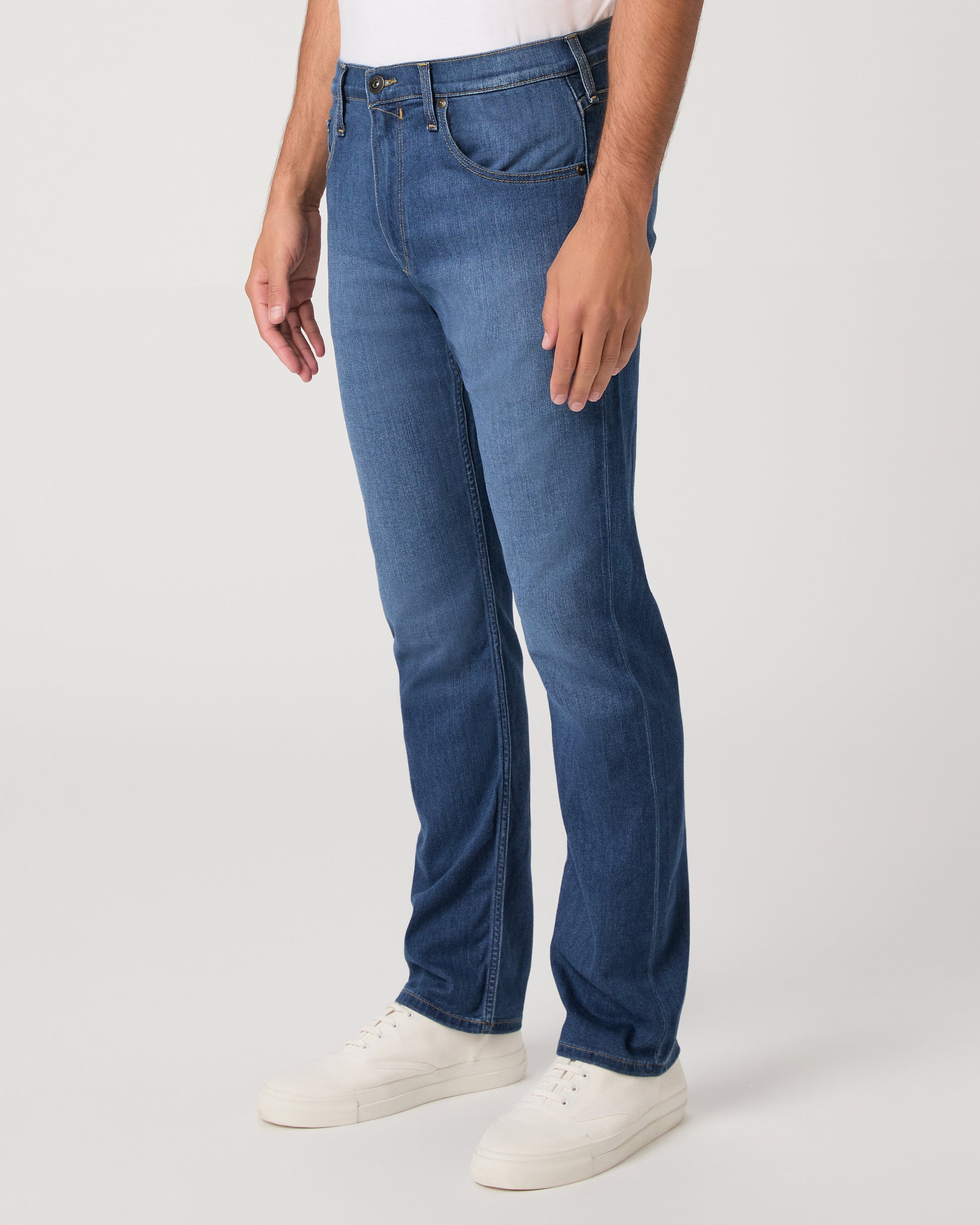Man wearing a white shirt, blue jeans, and white shoes on a white background