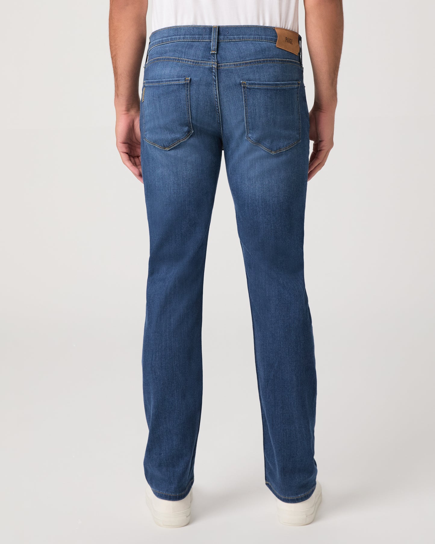 Man wearing a white shirt, blue jeans, and white shoes on a white background