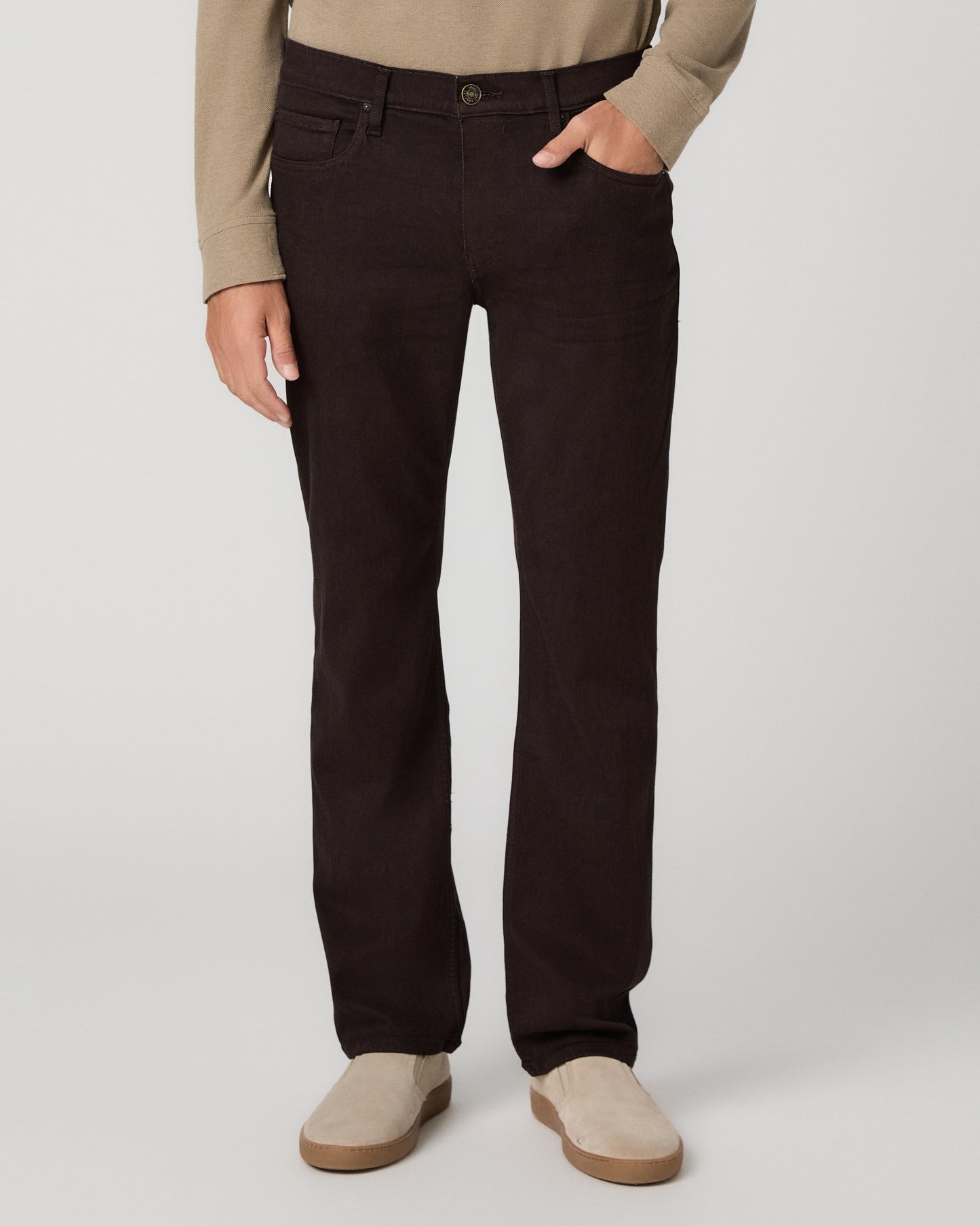 A man modeling a beige long-sleeve polo shirt with dark brown trousers and beige slip-on shoes, standing against a light gray studio background.