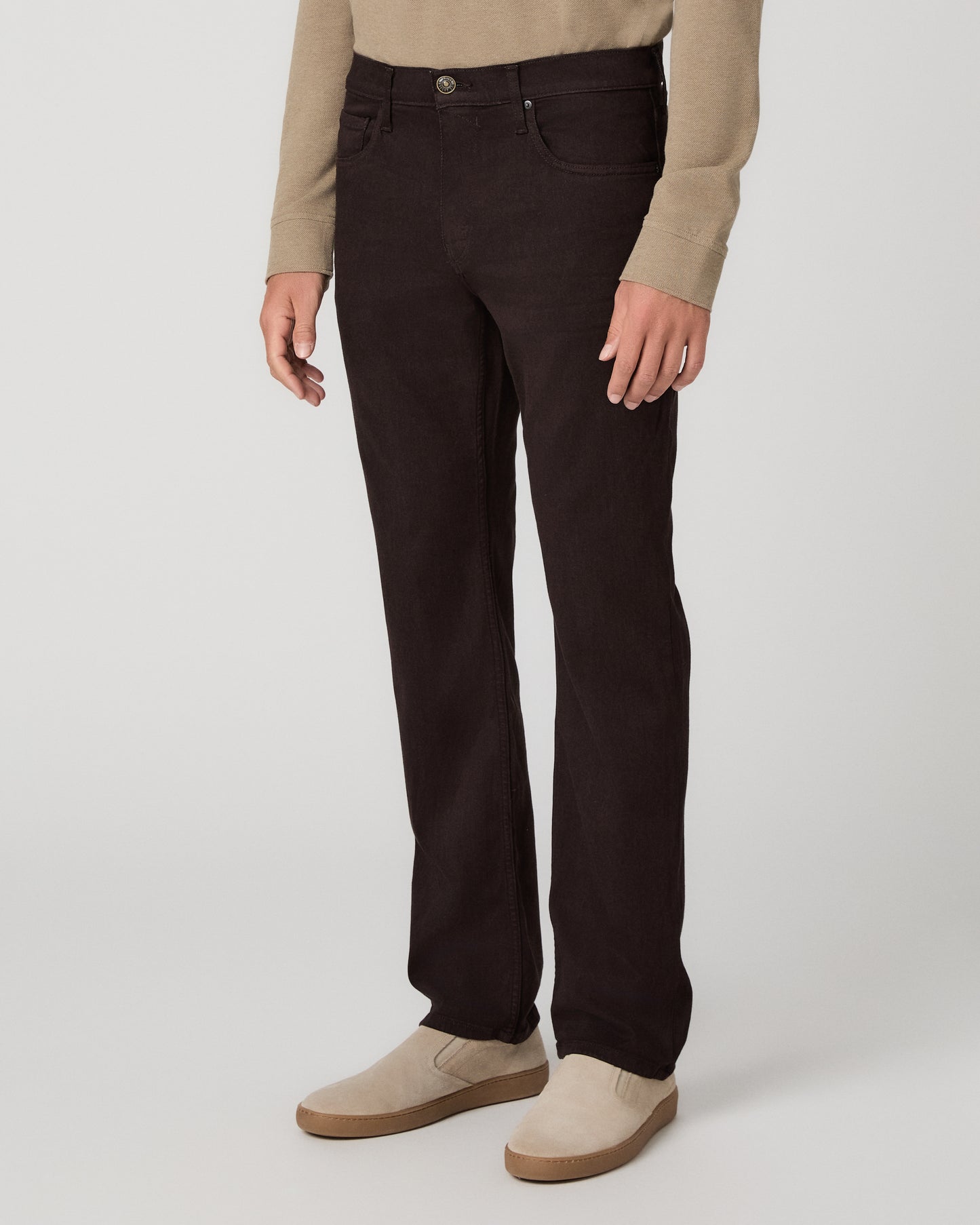 A man modeling a beige long-sleeve polo shirt with dark brown trousers and beige slip-on shoes, standing against a light gray studio background.
