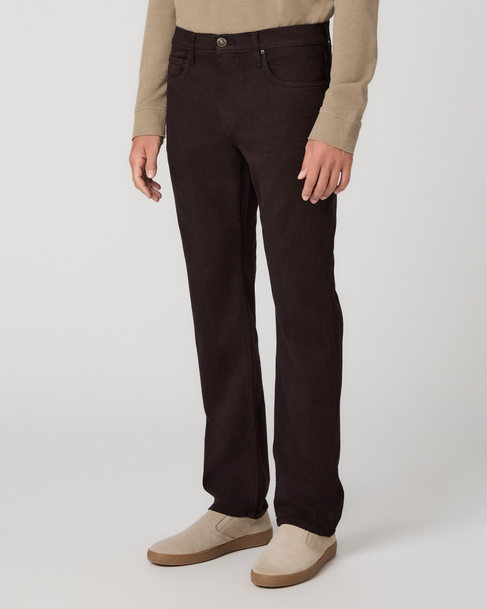 A man modeling a beige long-sleeve polo shirt with dark brown trousers and beige slip-on shoes, standing against a light gray studio background.