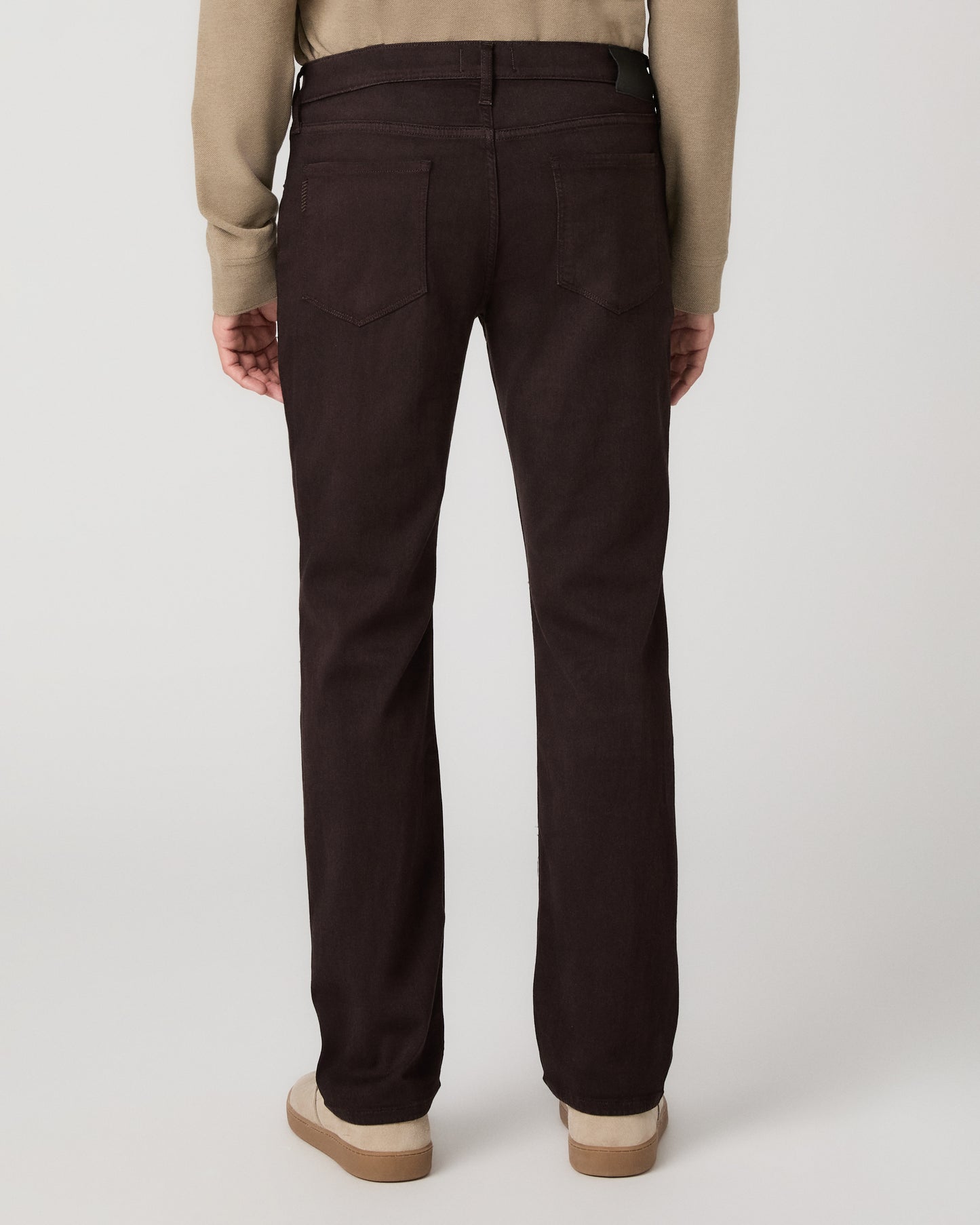 A man modeling a beige long-sleeve polo shirt with dark brown trousers and beige slip-on shoes, standing against a light gray studio background.