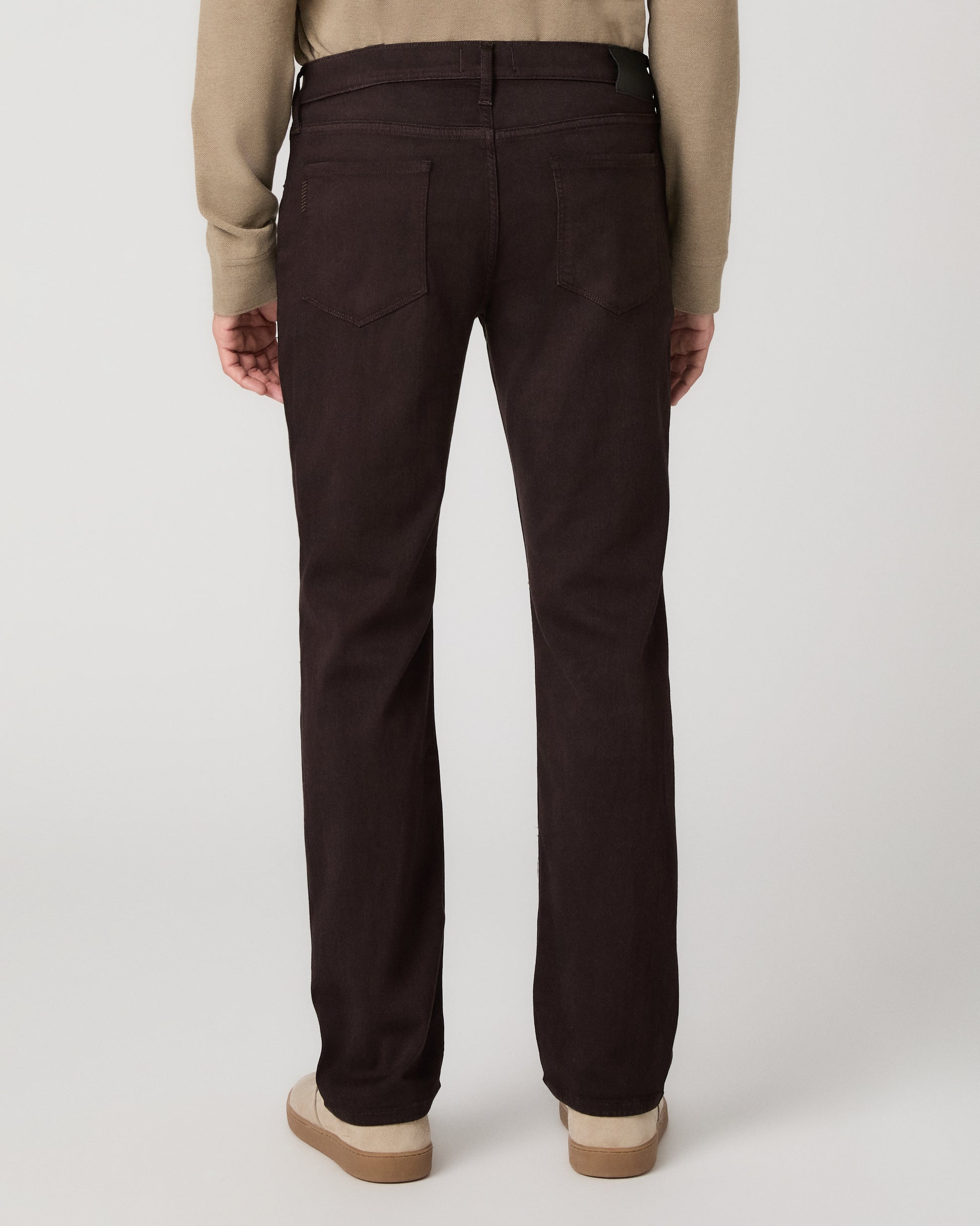 A man modeling a beige long-sleeve polo shirt with dark brown trousers and beige slip-on shoes, standing against a light gray studio background.