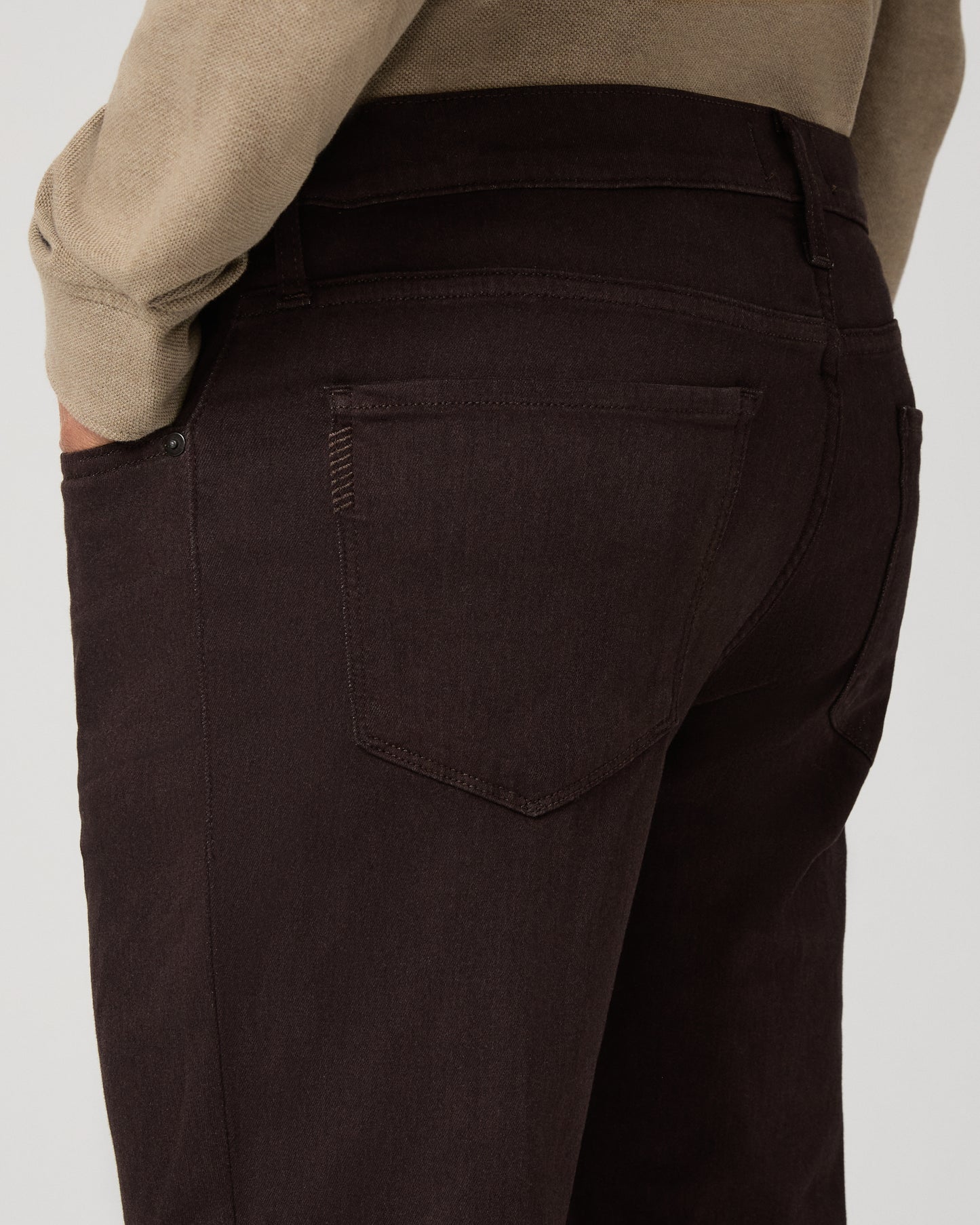 A man modeling a beige long-sleeve polo shirt with dark brown trousers, standing against a light gray studio background.