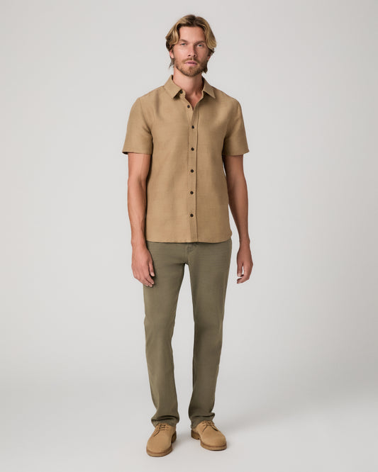 A man modeling a short-sleeve button-up shirt in tan and olive green pants, standing against a light gray studio background.