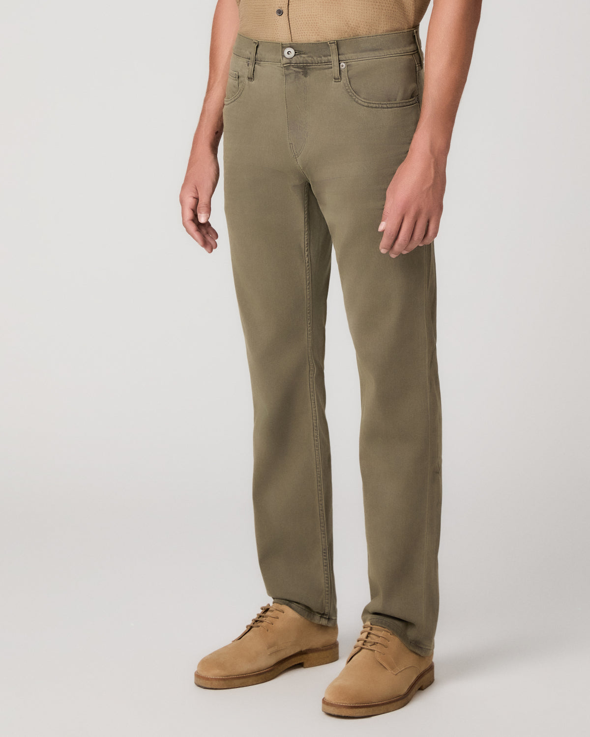 A man modeling a short-sleeve button-up shirt in tan and olive green pants, standing against a light gray studio background.