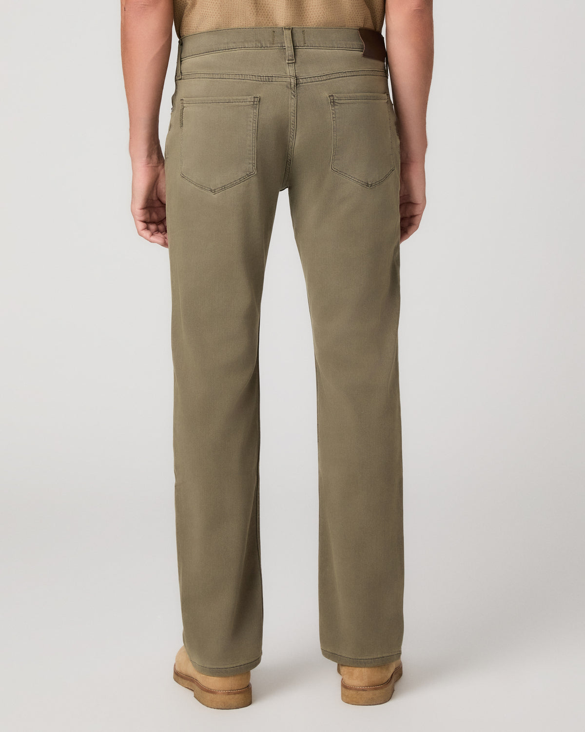 A man modeling a short-sleeve button-up shirt in tan and olive green pants, standing against a light gray studio background.