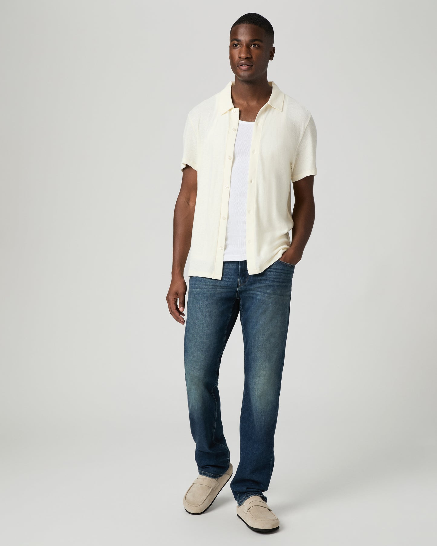 Man wearing a white shirt, blue jeans, and beige shoes on a plain background