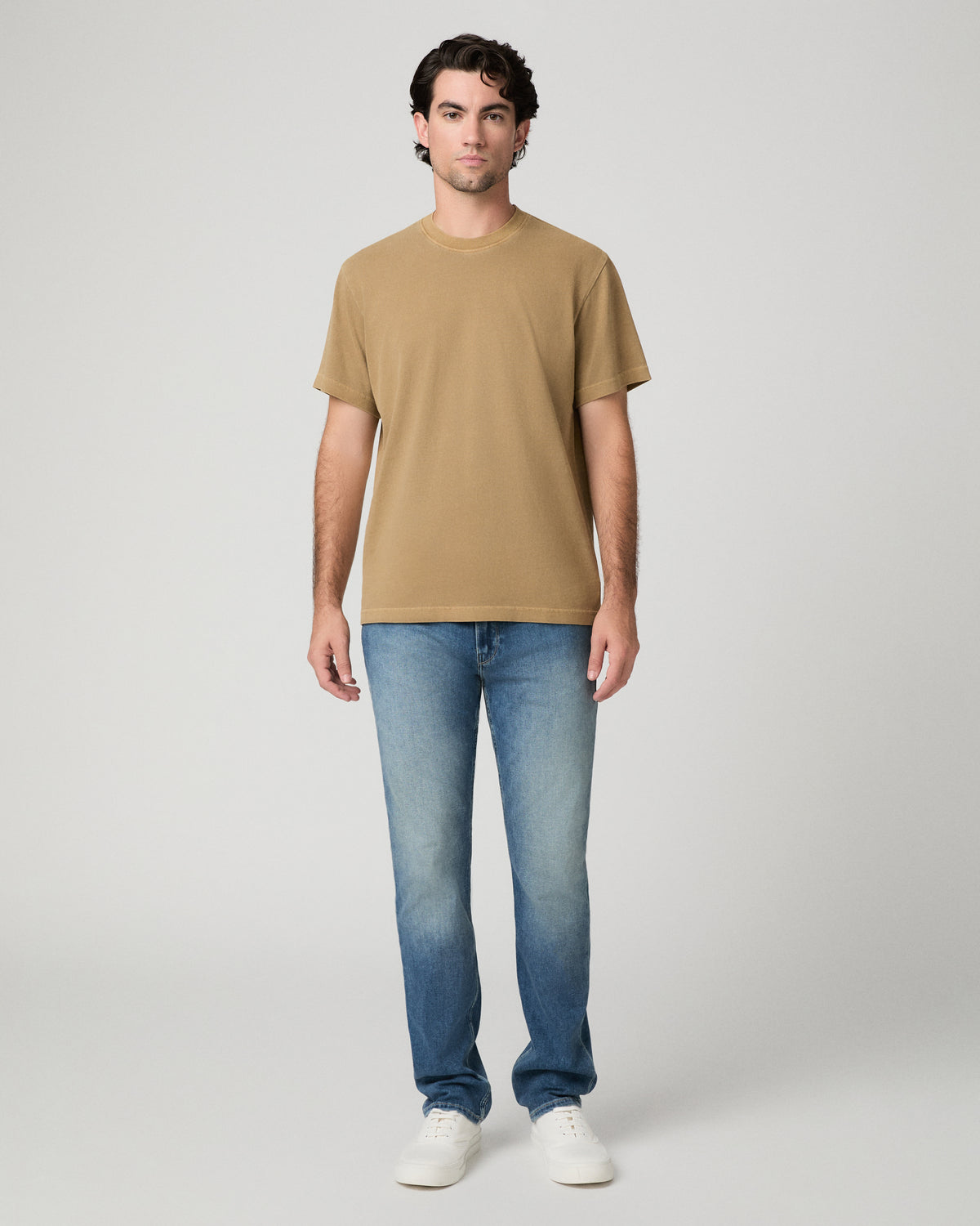 Man wearing beige top and light jeans against a white background