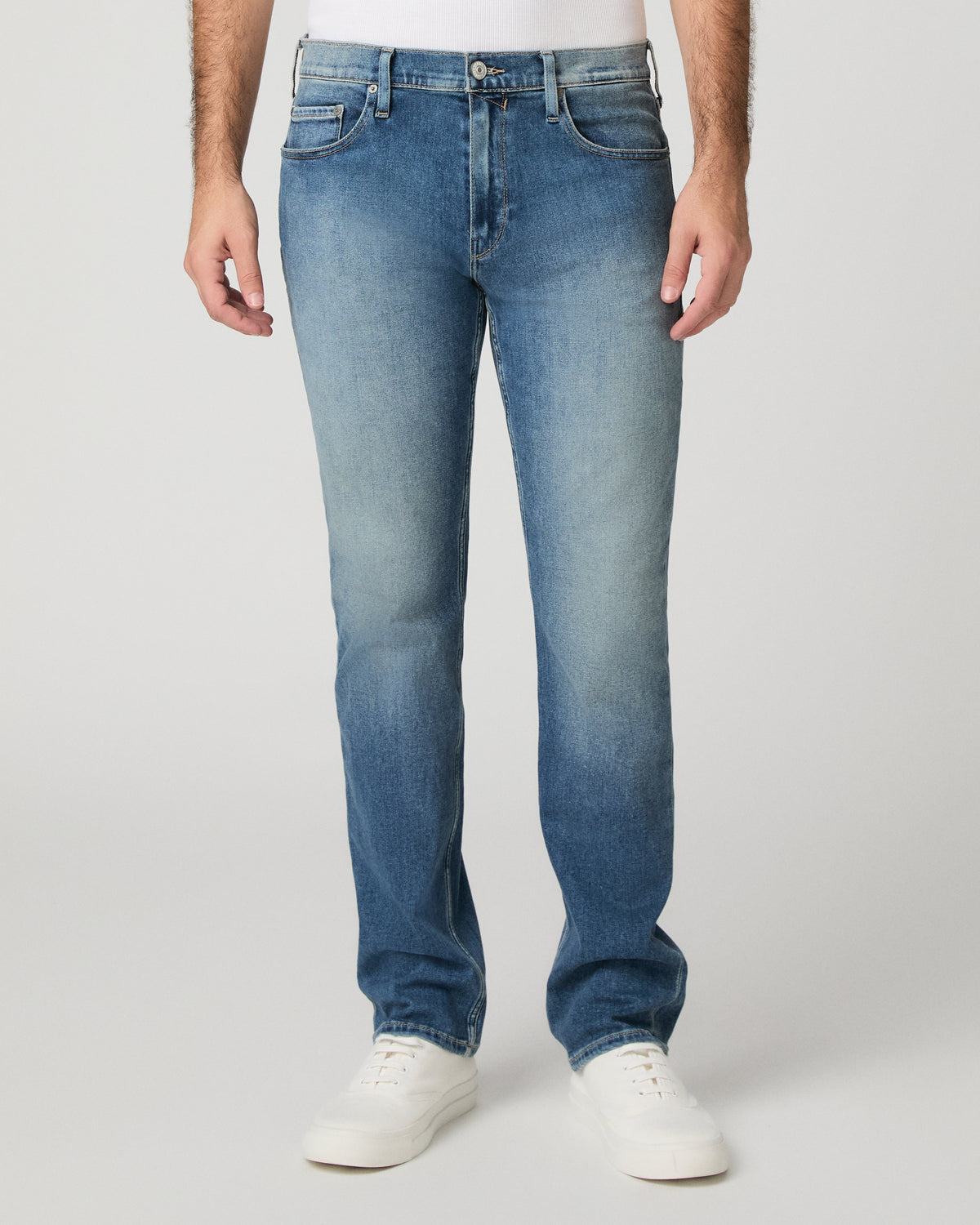 Man wearing white top and light jeans against a white background