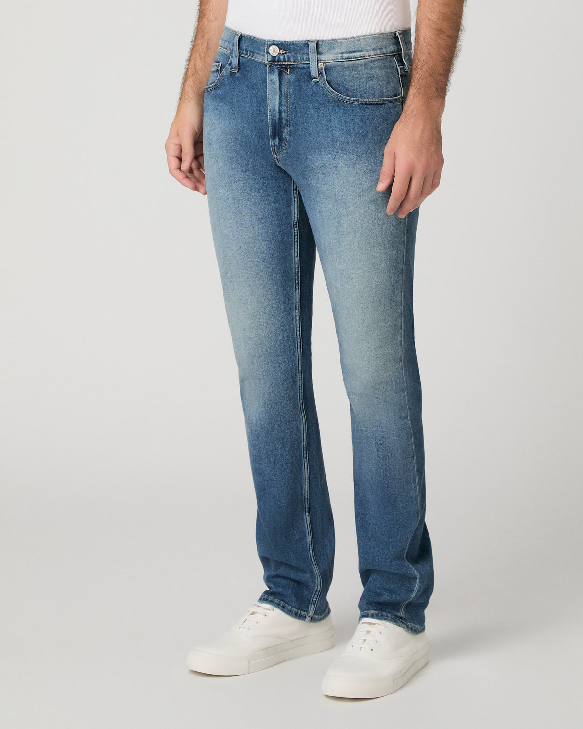 Man wearing white top and light jeans against a white background