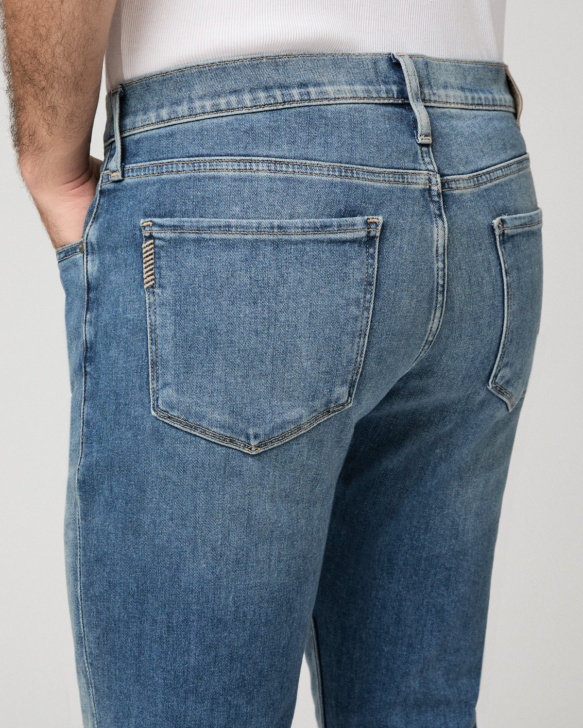 Man wearing white top and light jeans against a white background