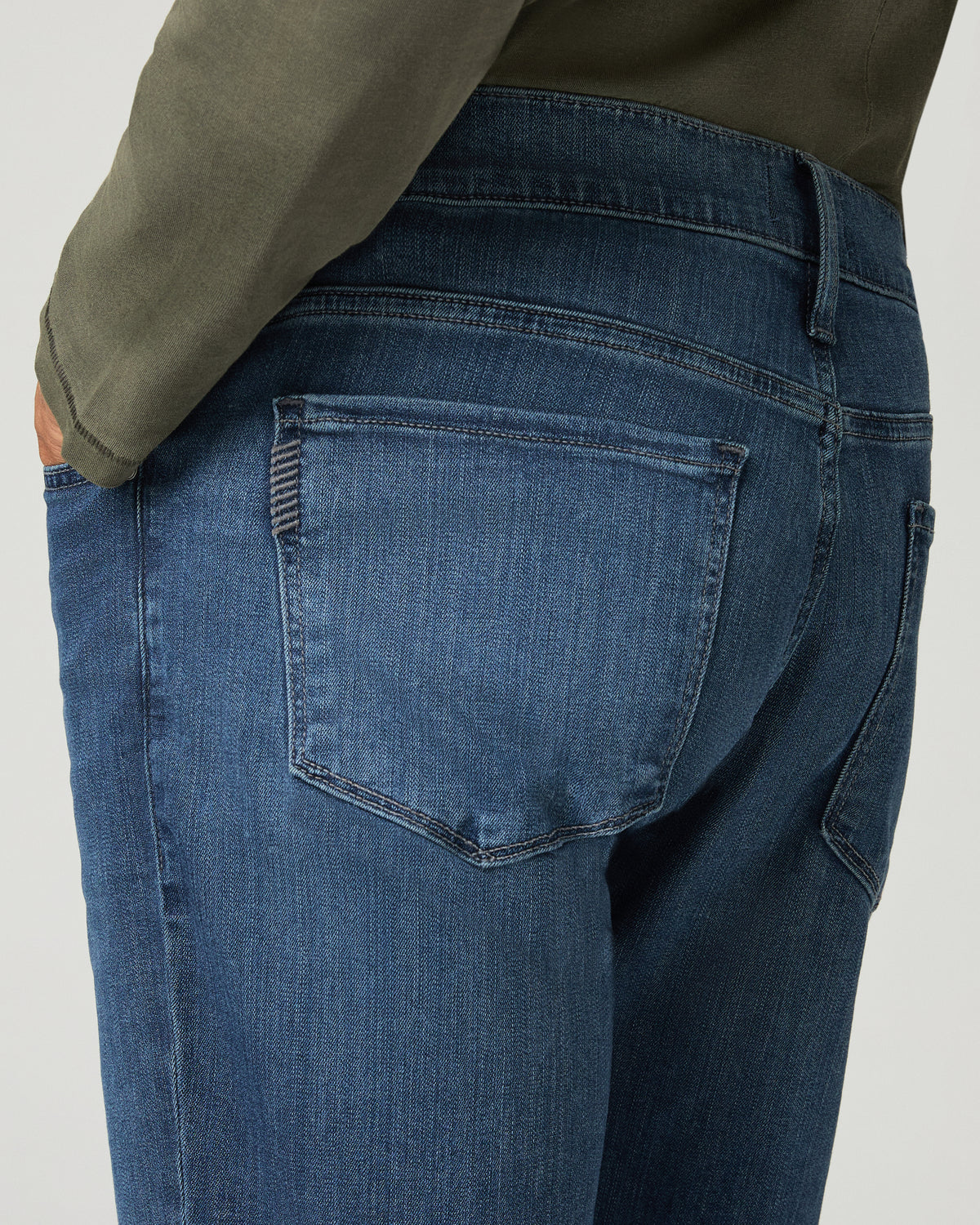 Close-up of the back pocket and belt loops on the medium blue wash denim, hand tucked into the pocket.