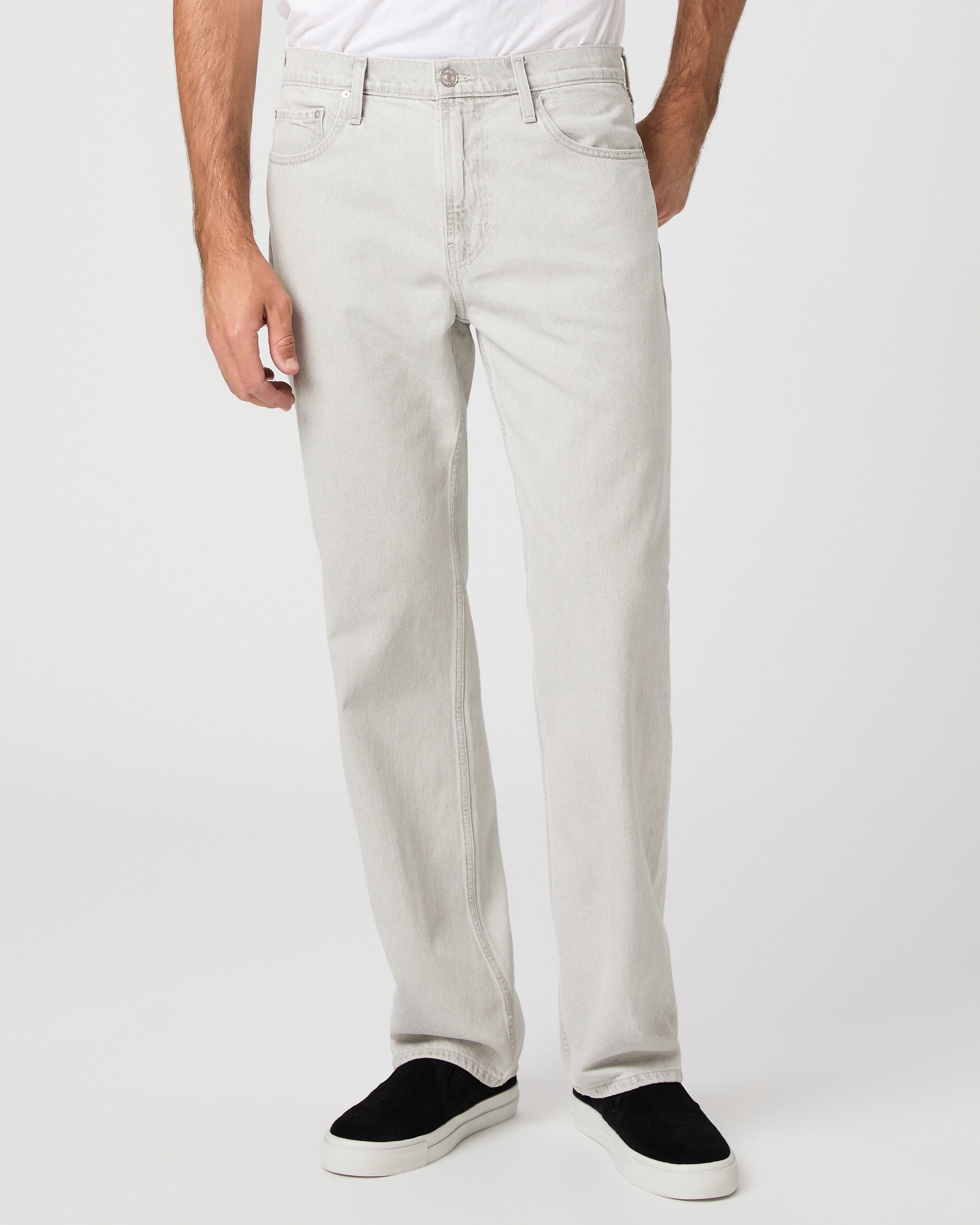 Man wearing a white tee and grey pants paired with black sneakers on a white background