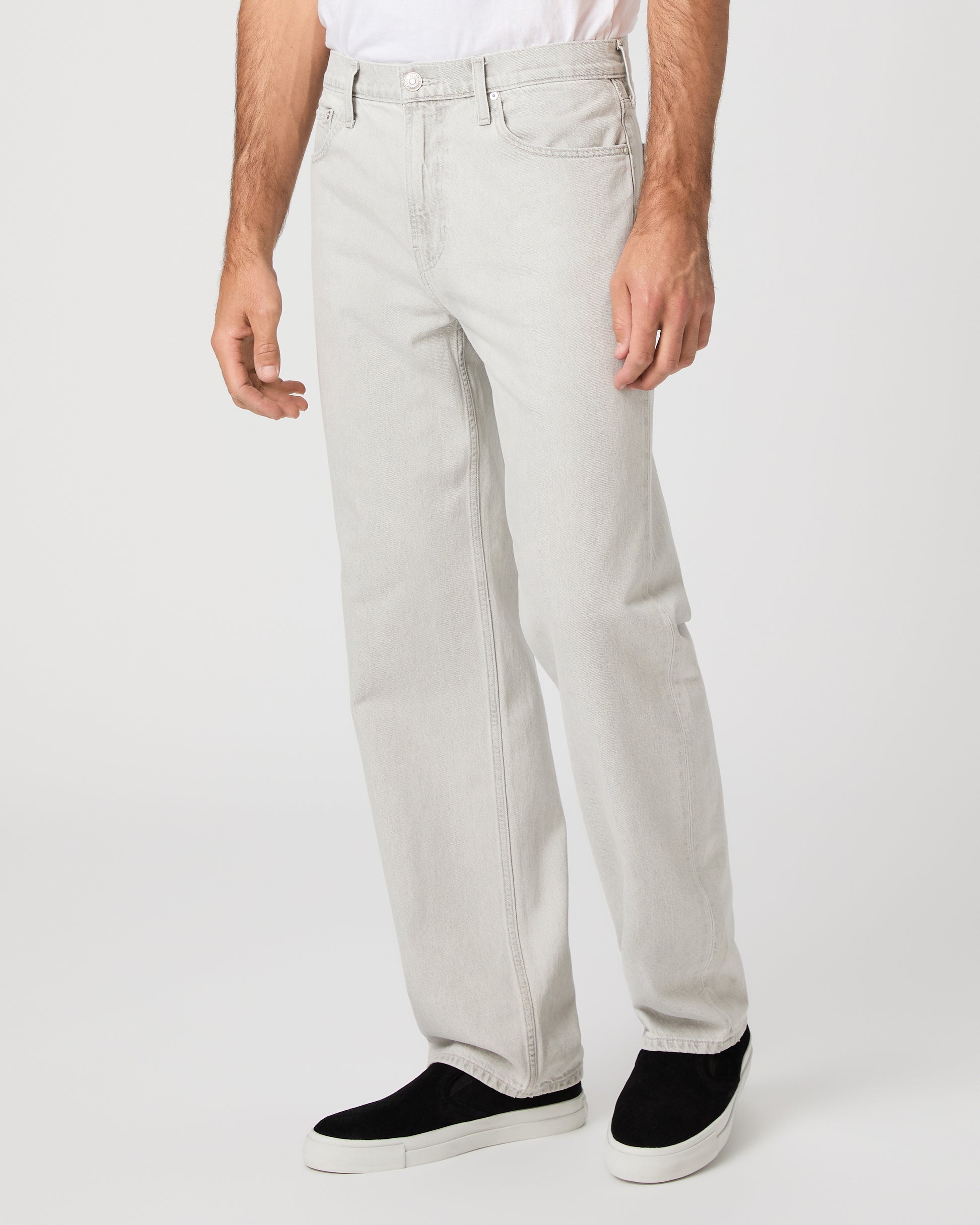 Man wearing a white tee and grey pants paired with black sneakers on a white background