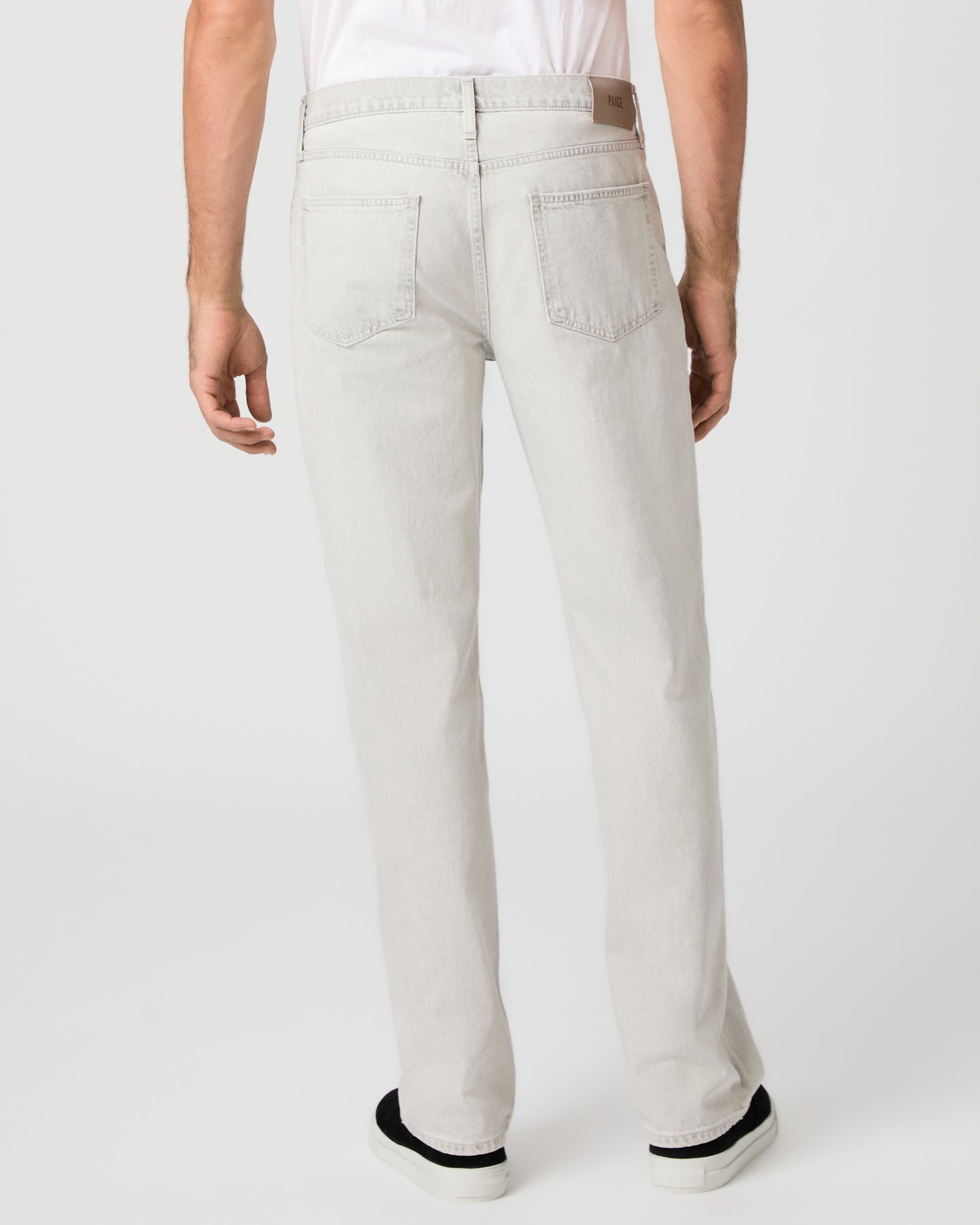 Man wearing a white tee and grey pants paired with black sneakers on a white background