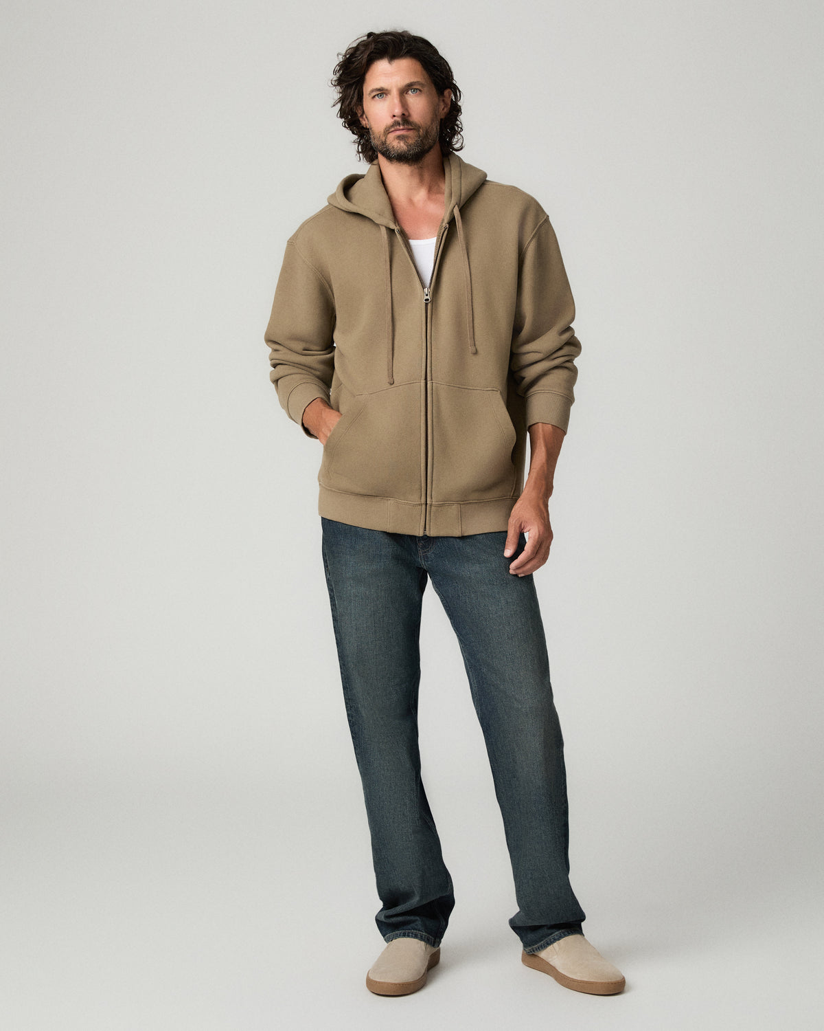 Full-length front view of a man wearing a tan suede shacket over a white tee, paired with dark indigo Whitaker-wash relaxed straight jeans featuring heavy heritage-style whiskering, and tan suede boots, standing with arms relaxed at his sides.