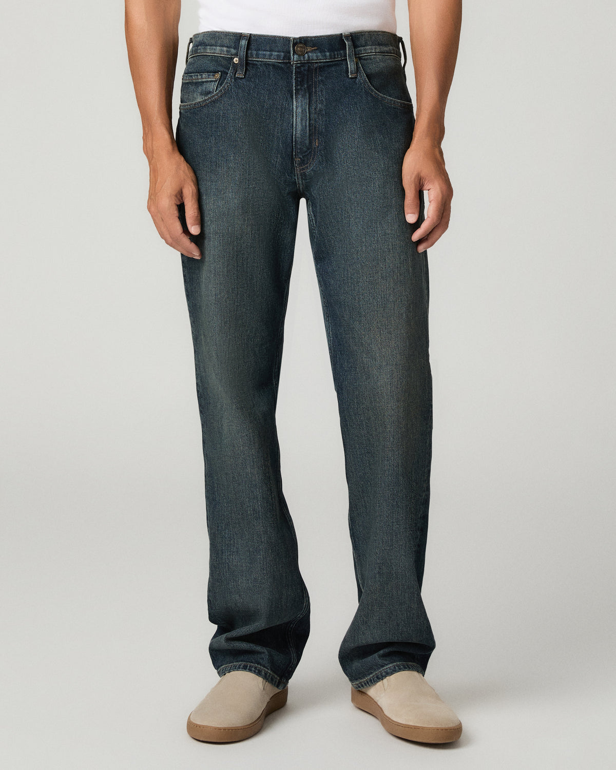 Close front view from the waist down of the heavily washed dark indigo relaxed straight jeans, showing pronounced whiskering across the thighs, worn with tan suede boots.
