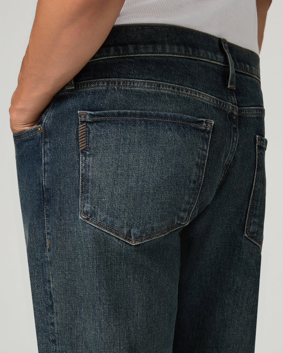 Close-up of the back pocket and yoke stitching on the heavily washed denim, hand resting in the back pocket.
