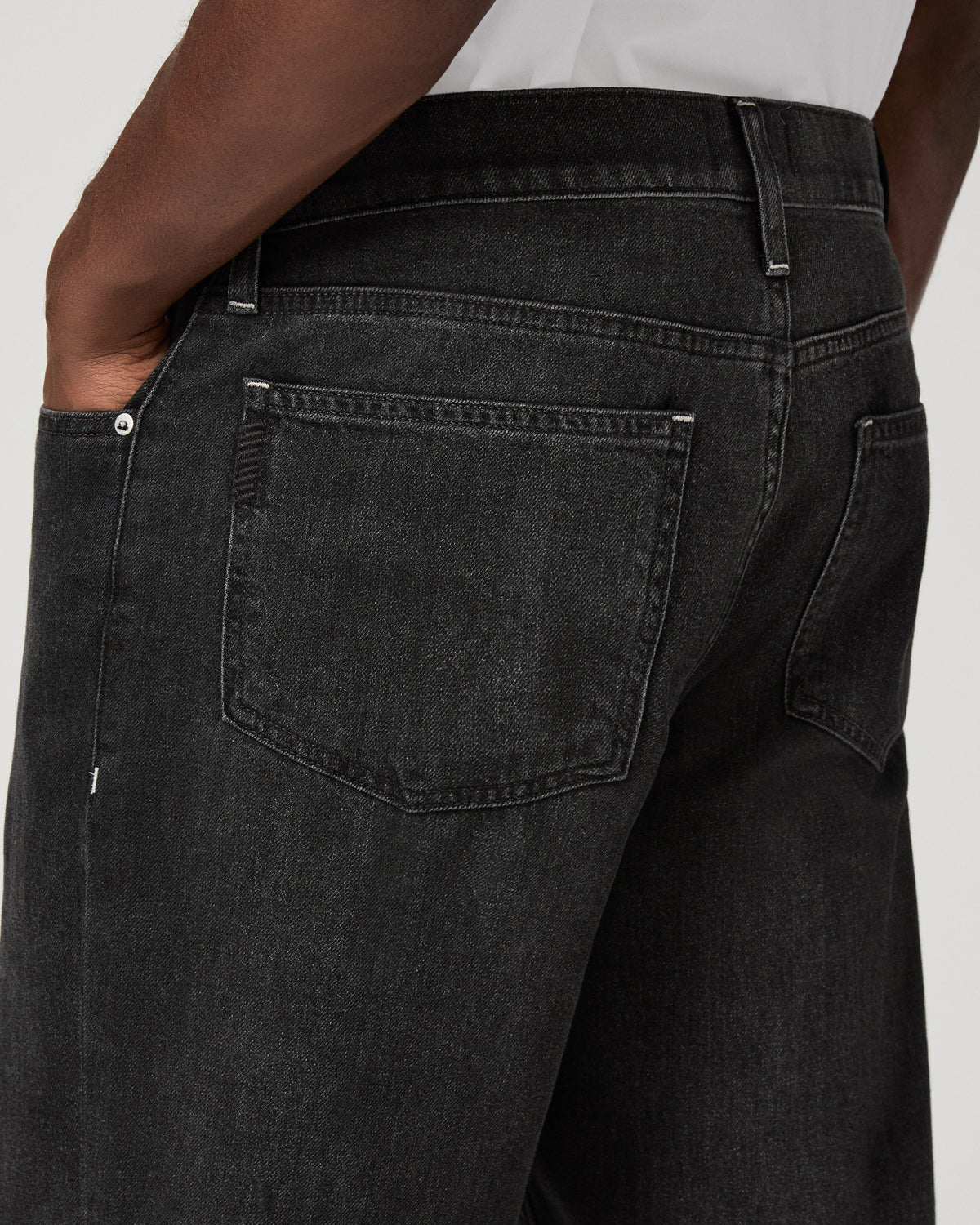 Close-up of the back pocket detailing on the charcoal-black denim, hand tucked into the pocket.