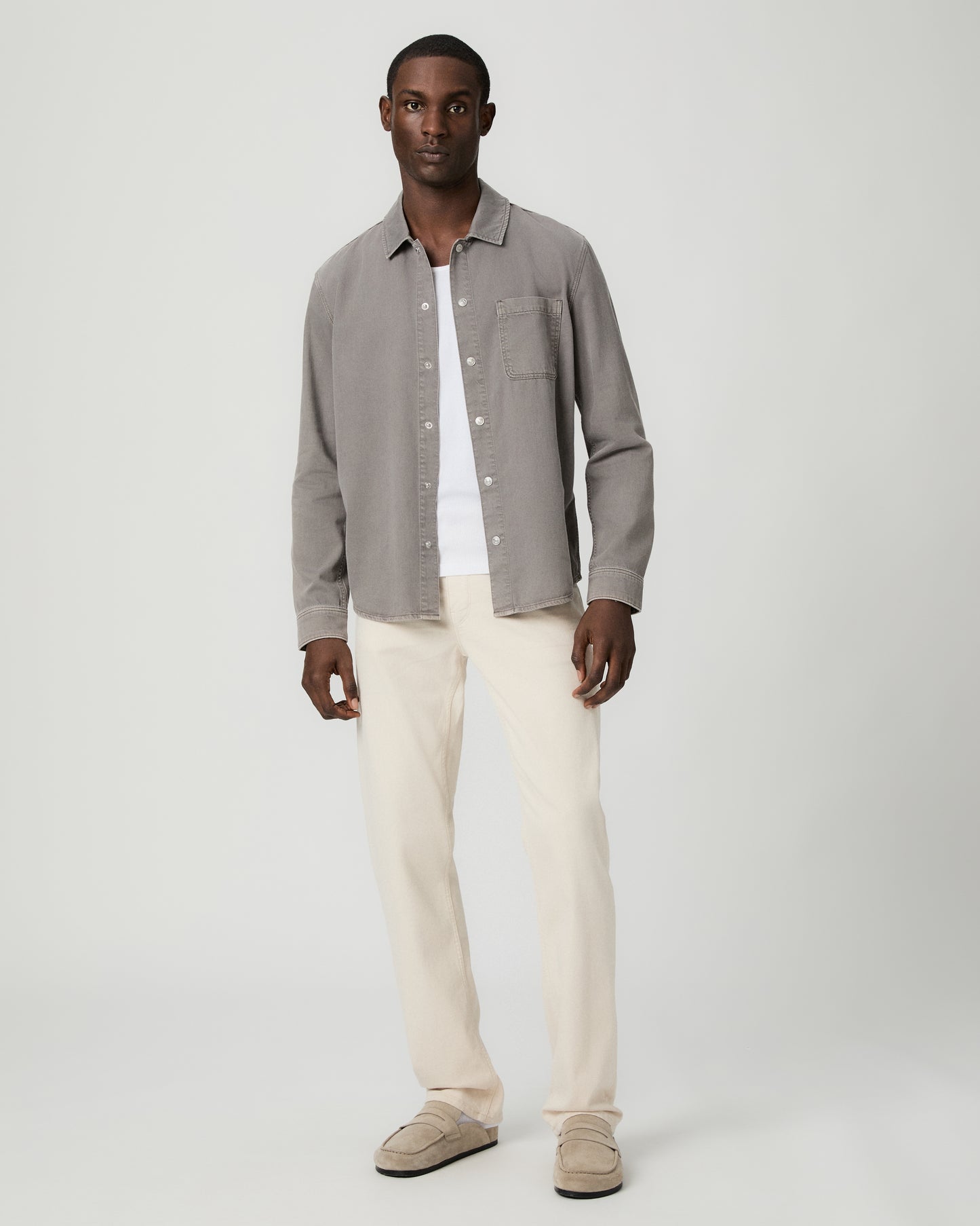 Man wearing a gray button-up shirt with a pocket and white pants on a white background