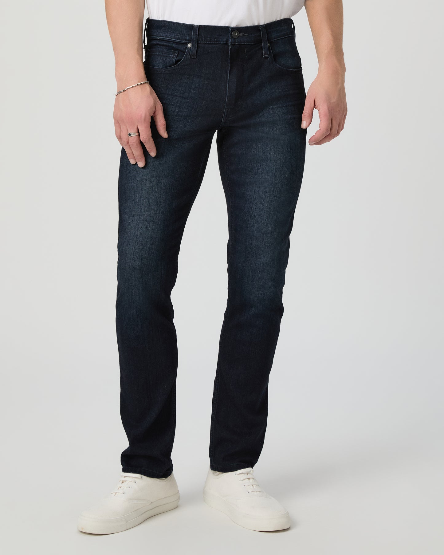 Person wearing dark blue jeans and white shoes on a light gray background