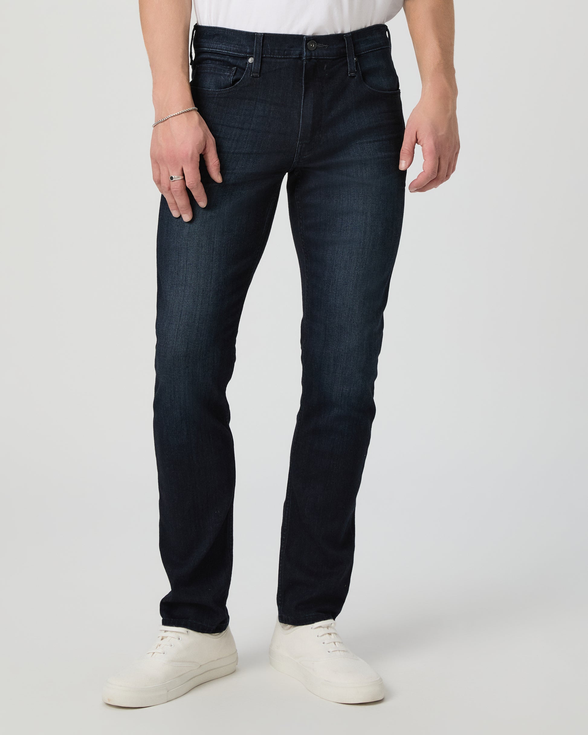 Person wearing dark blue jeans and white shoes on a light gray background