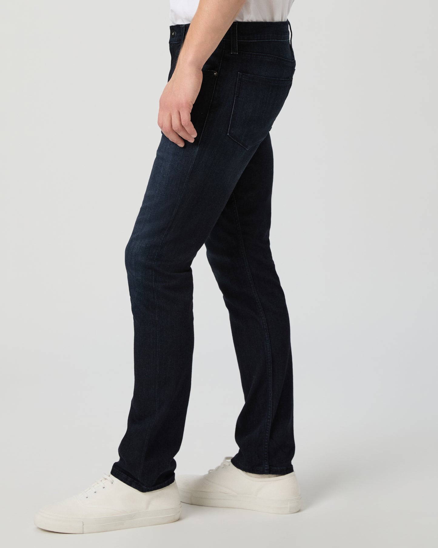 Person wearing dark blue jeans and white shoes on a light gray background