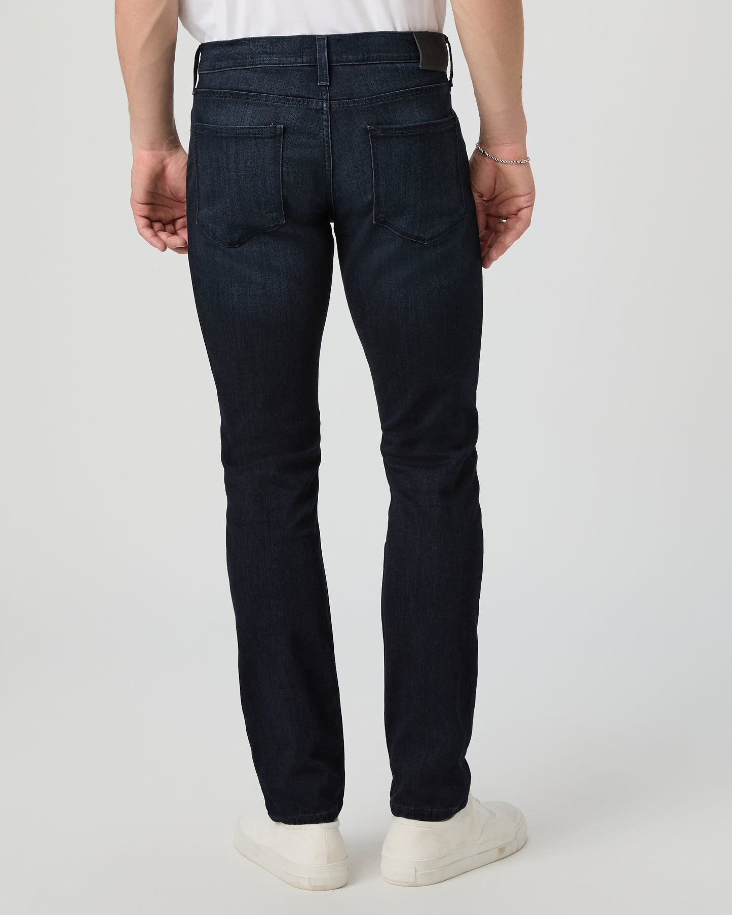 Person wearing dark blue jeans and white shoes on a light gray background